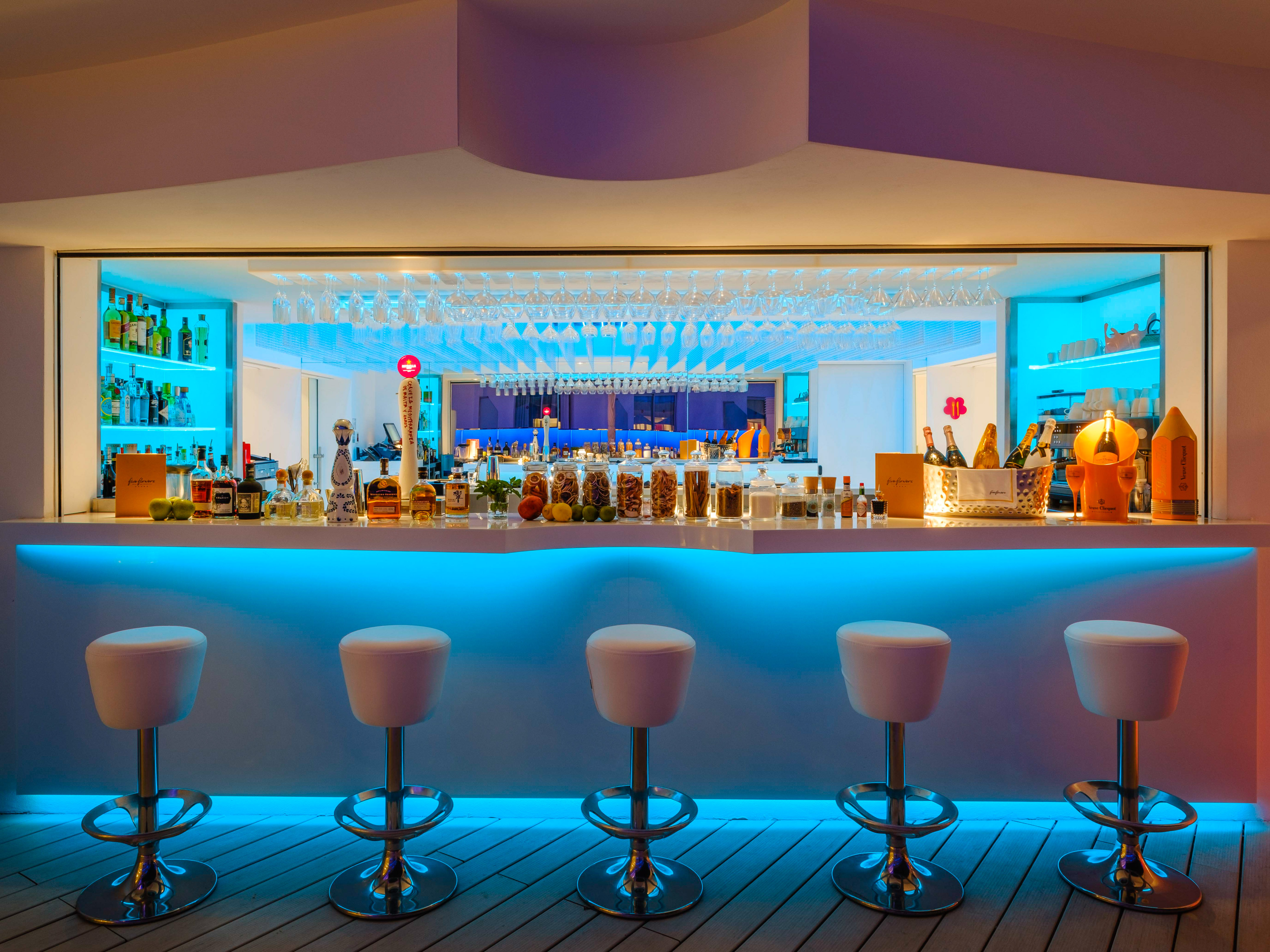Modern bar with blue LED lighting, white stools, and liquor bottles.