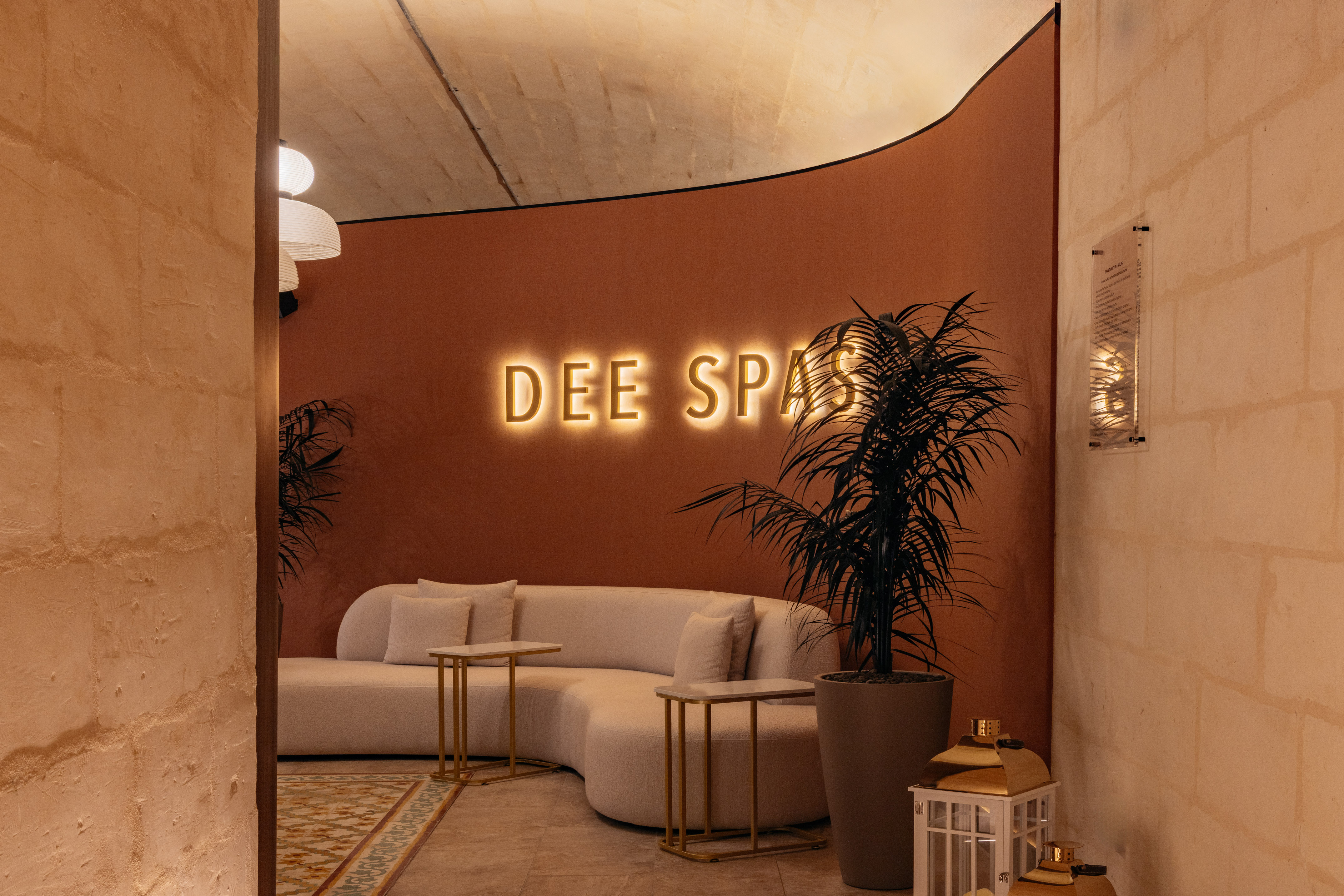 Luxurious DEE SPA reception with glowing sign, curved sofa, plant, and modern decor.