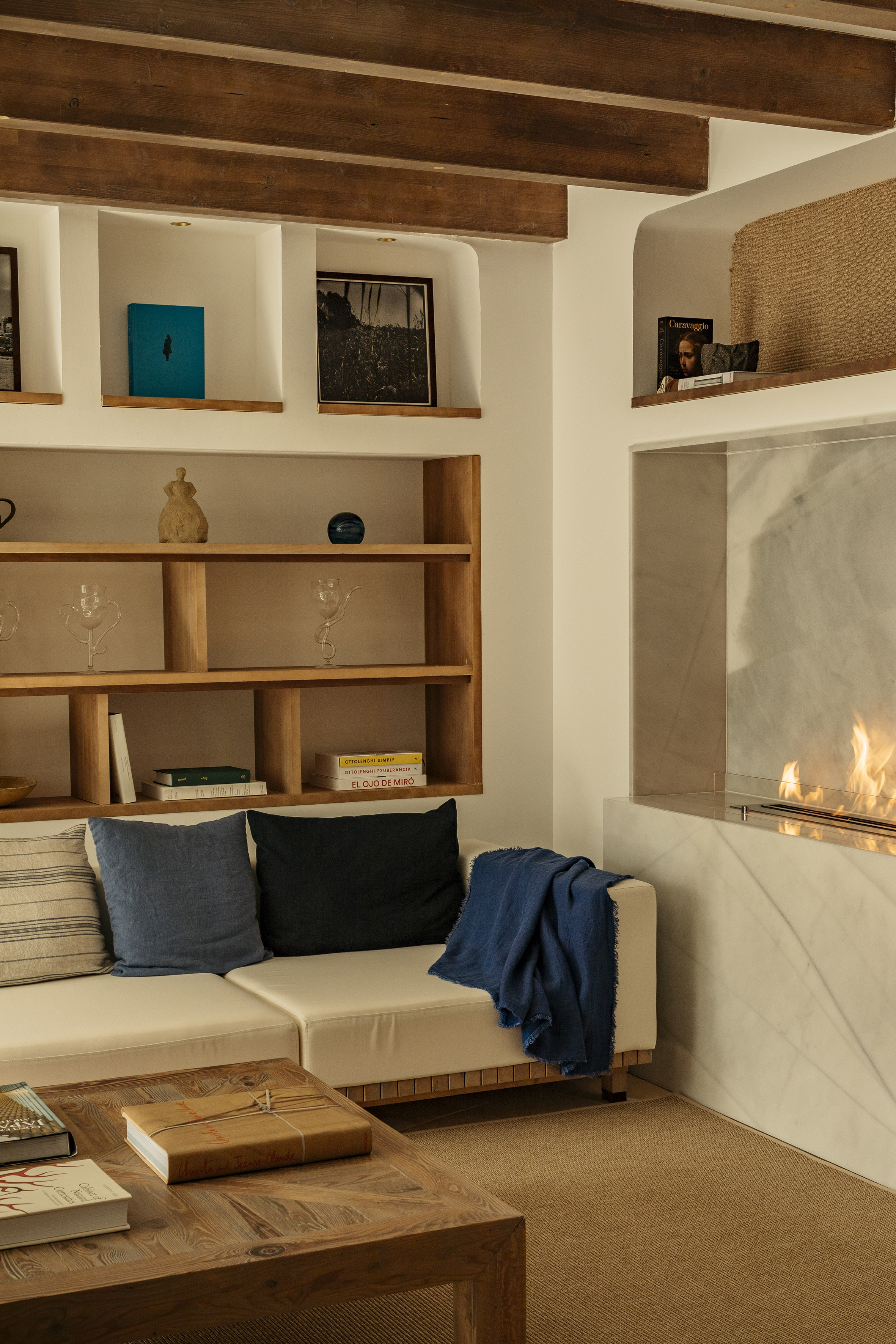 Modern living room: beige sofa, fireplace, wood shelves, exposed beams.