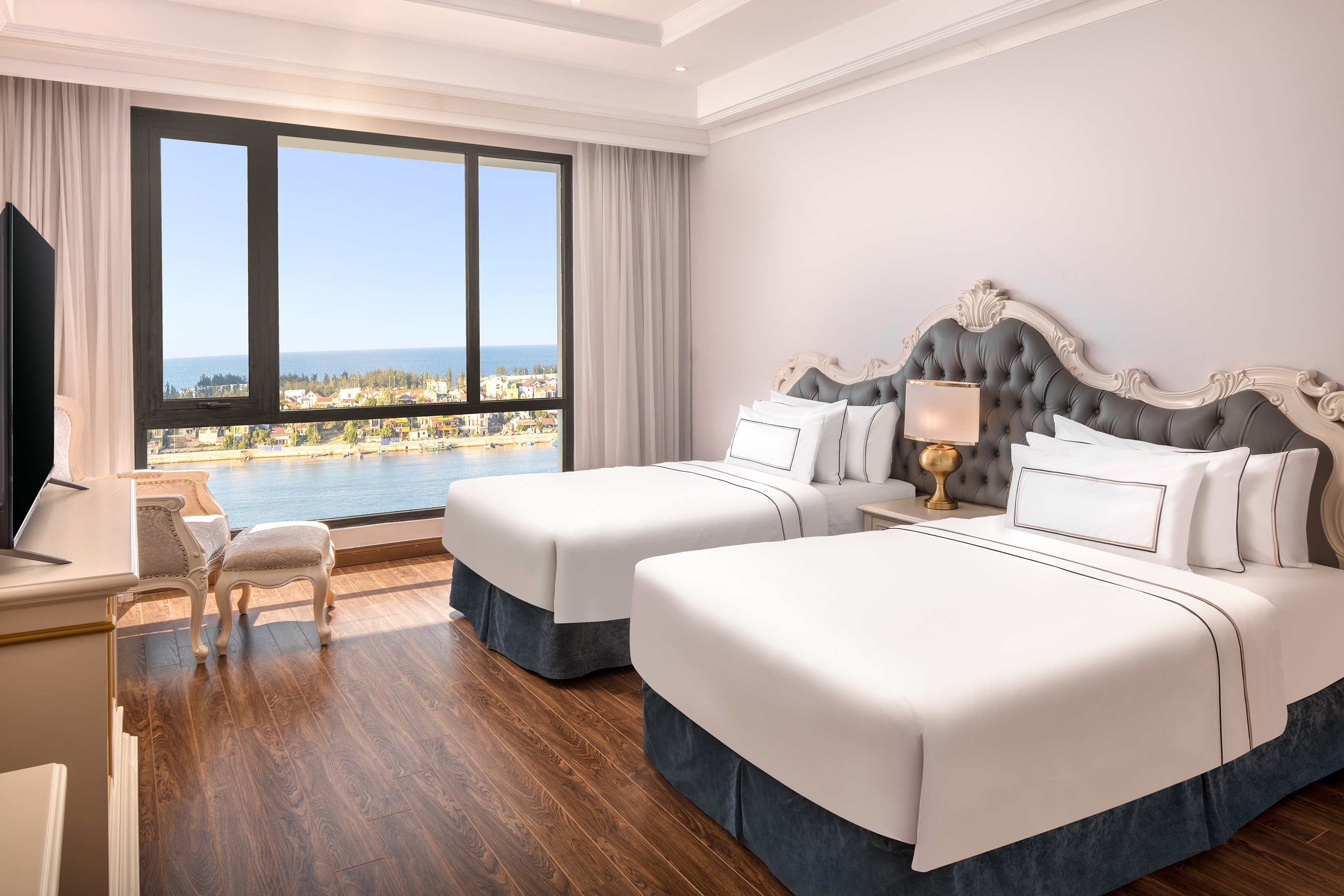 Elegant hotel room with twin beds, river, and ocean view from large window.