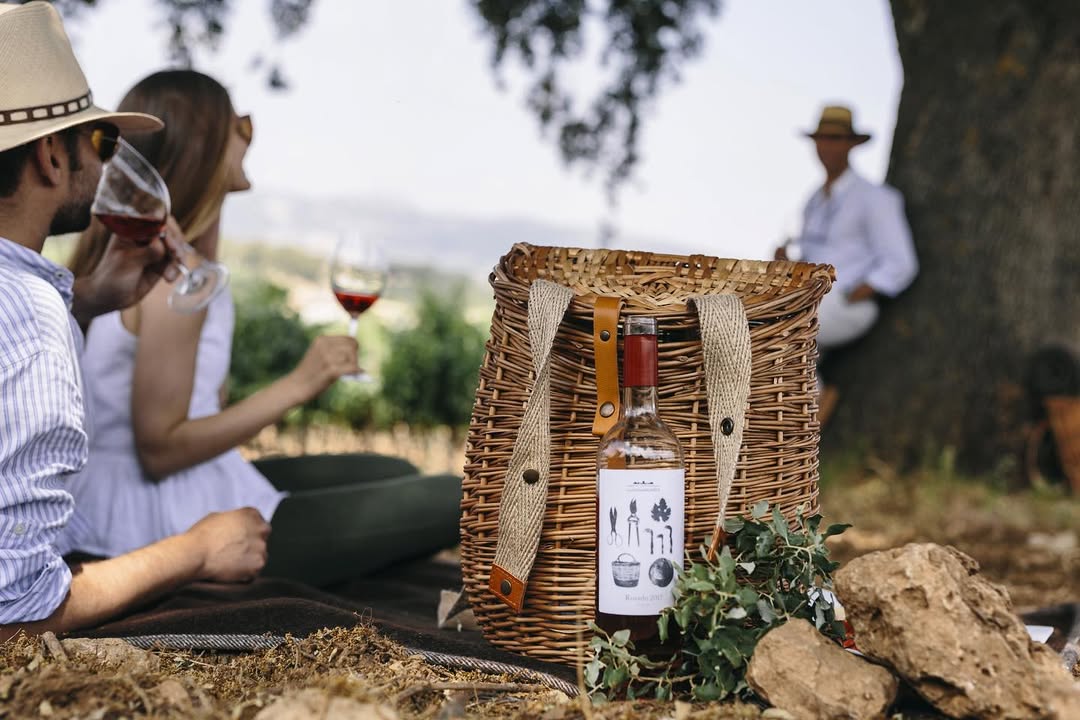 a picnic basket with a bottle of wine and a couple of people sitting on the ground