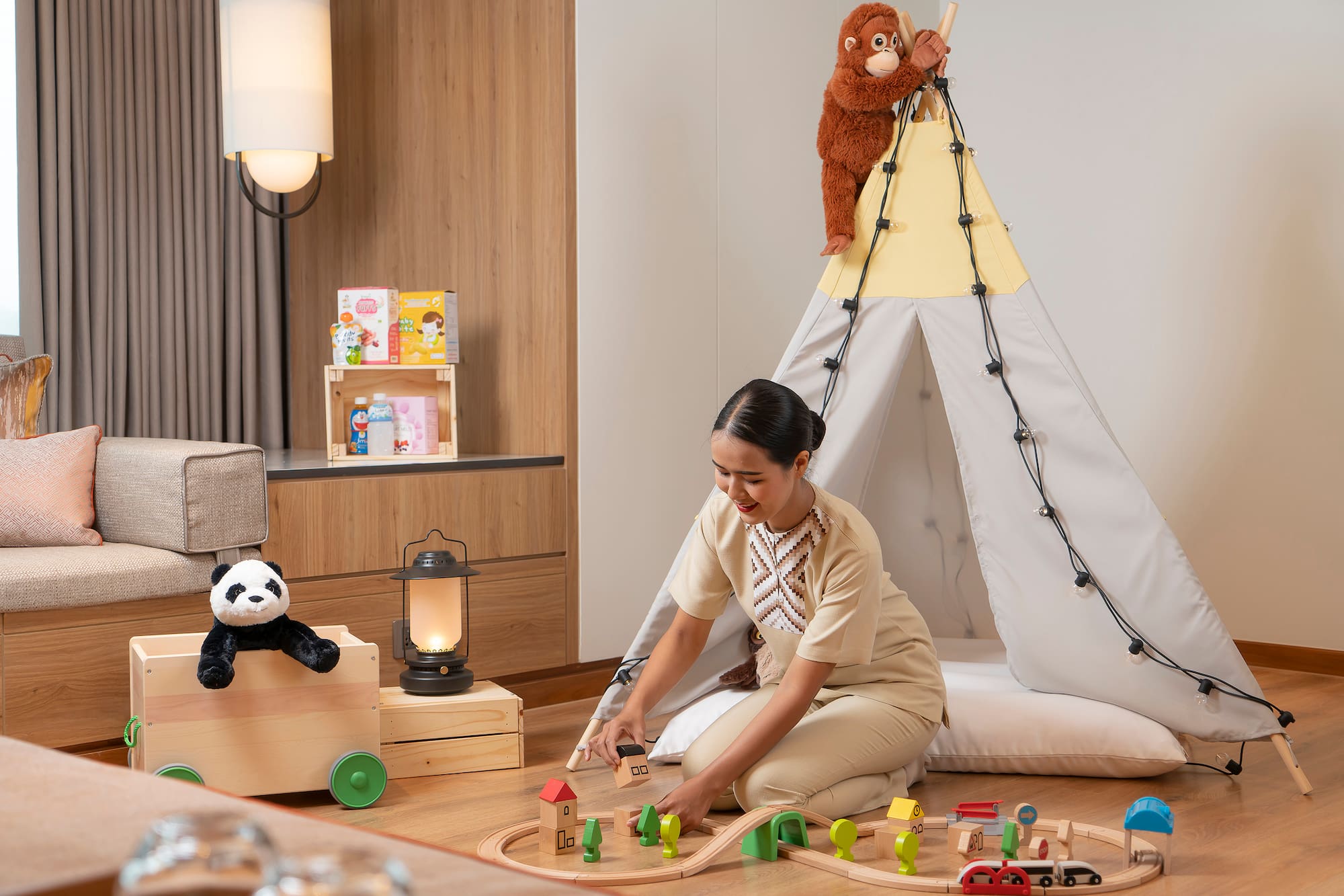 Woman plays with wooden train set, teepee, panda, orangutan toys in kids' room.
