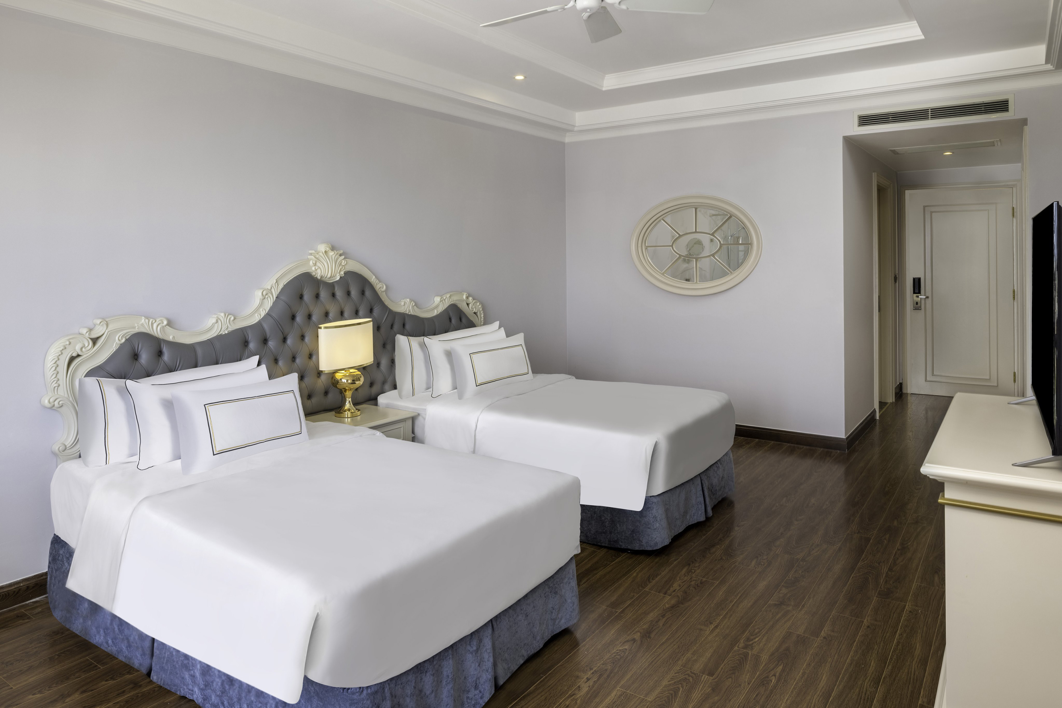 Elegant hotel room with two twin beds, ornate headboards, and gold accents.