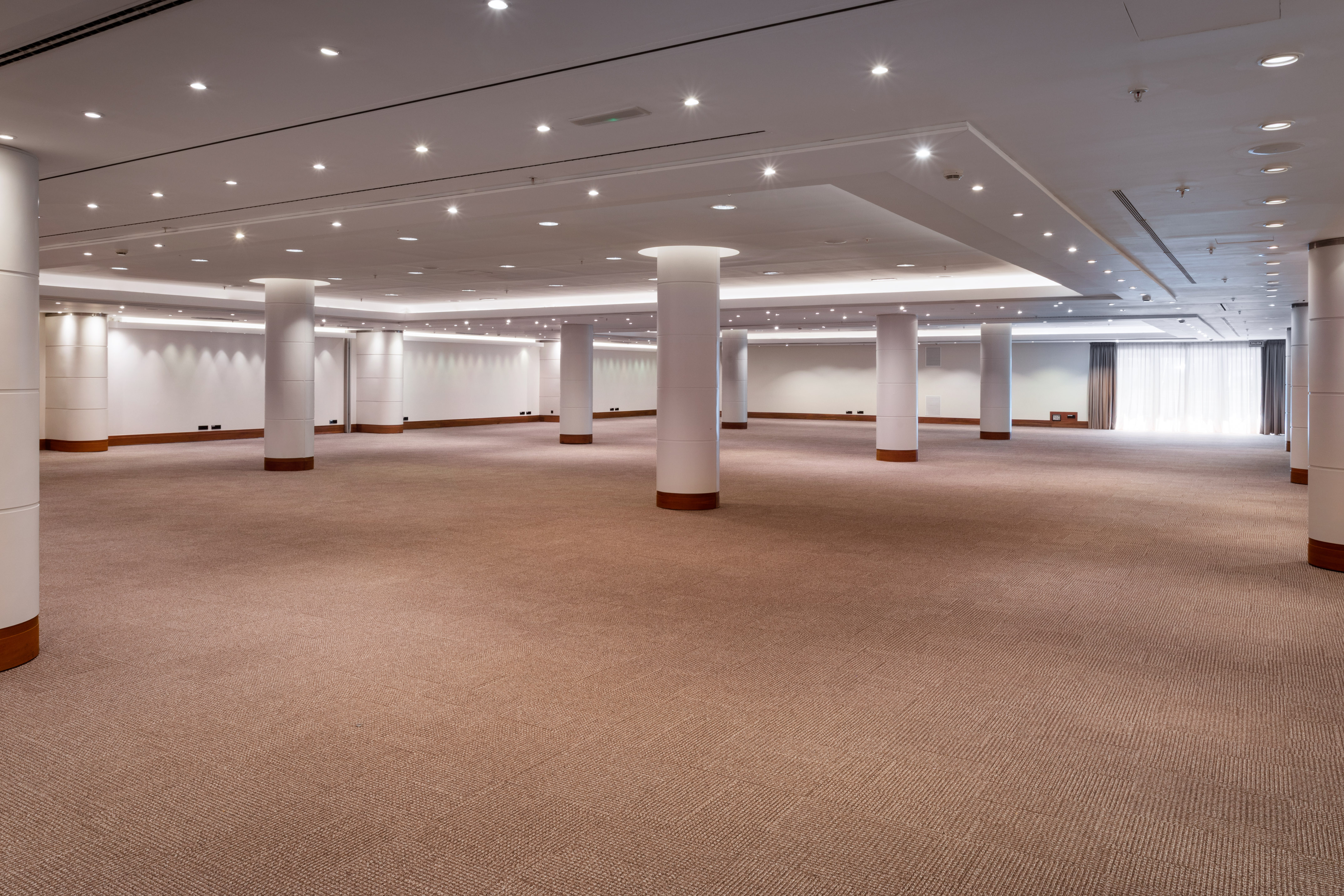 Empty large modern event space with carpeted floor, white columns, and bright lighting.