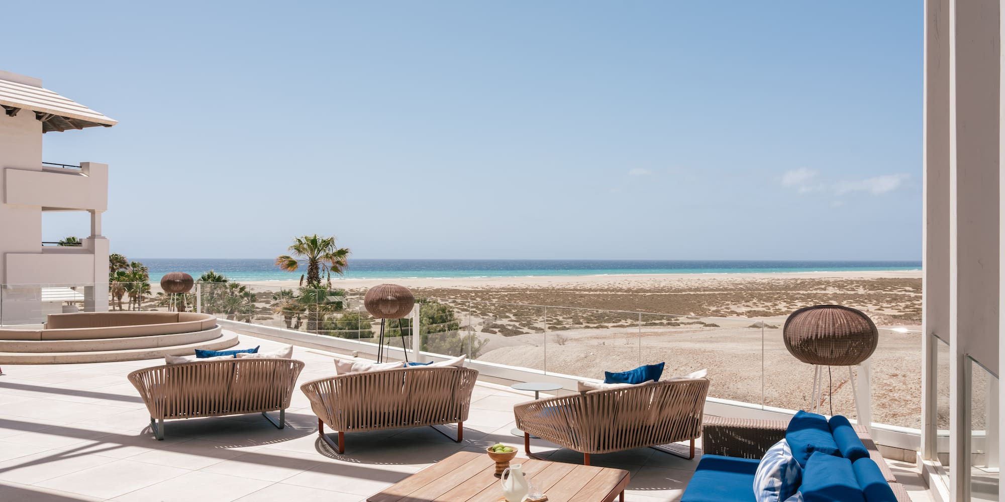 Beachfront resort patio with modern lounge furniture and ocean view.