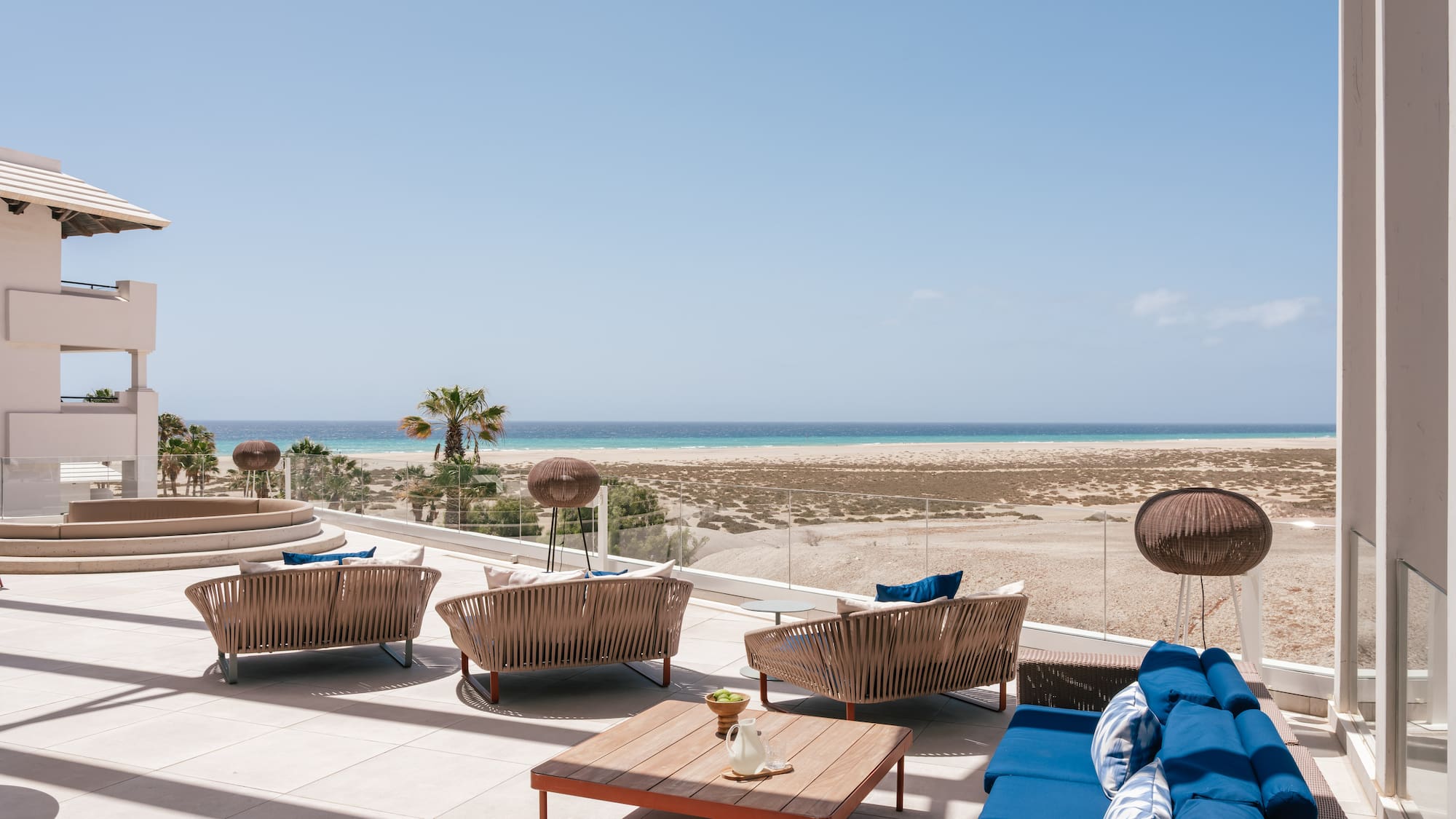 Oceanfront patio with modern outdoor furniture, sandy beach, and blue sea.