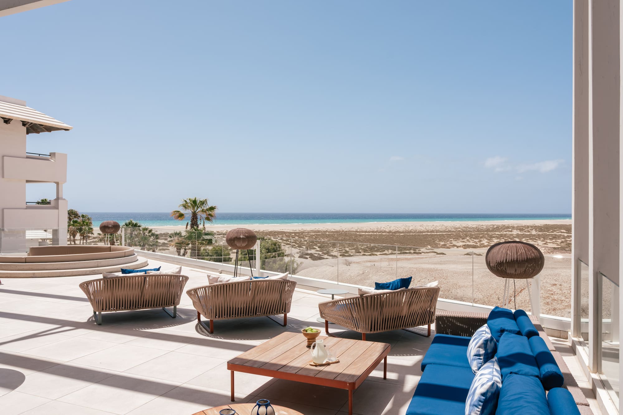 Beachfront resort patio with modern lounge furniture and ocean view.