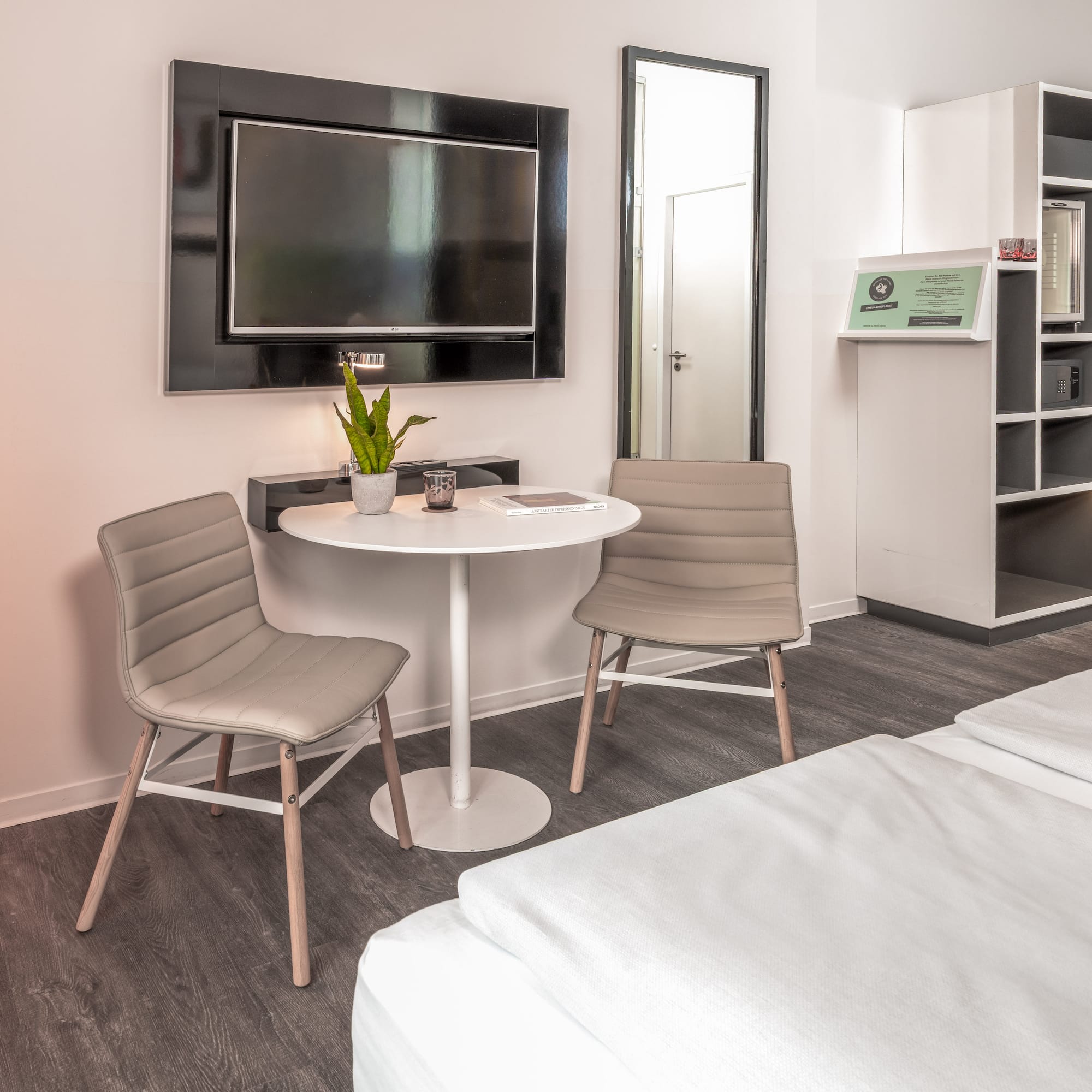 Modern hotel room with twin beds, small table, wall TV, and open wardrobe.