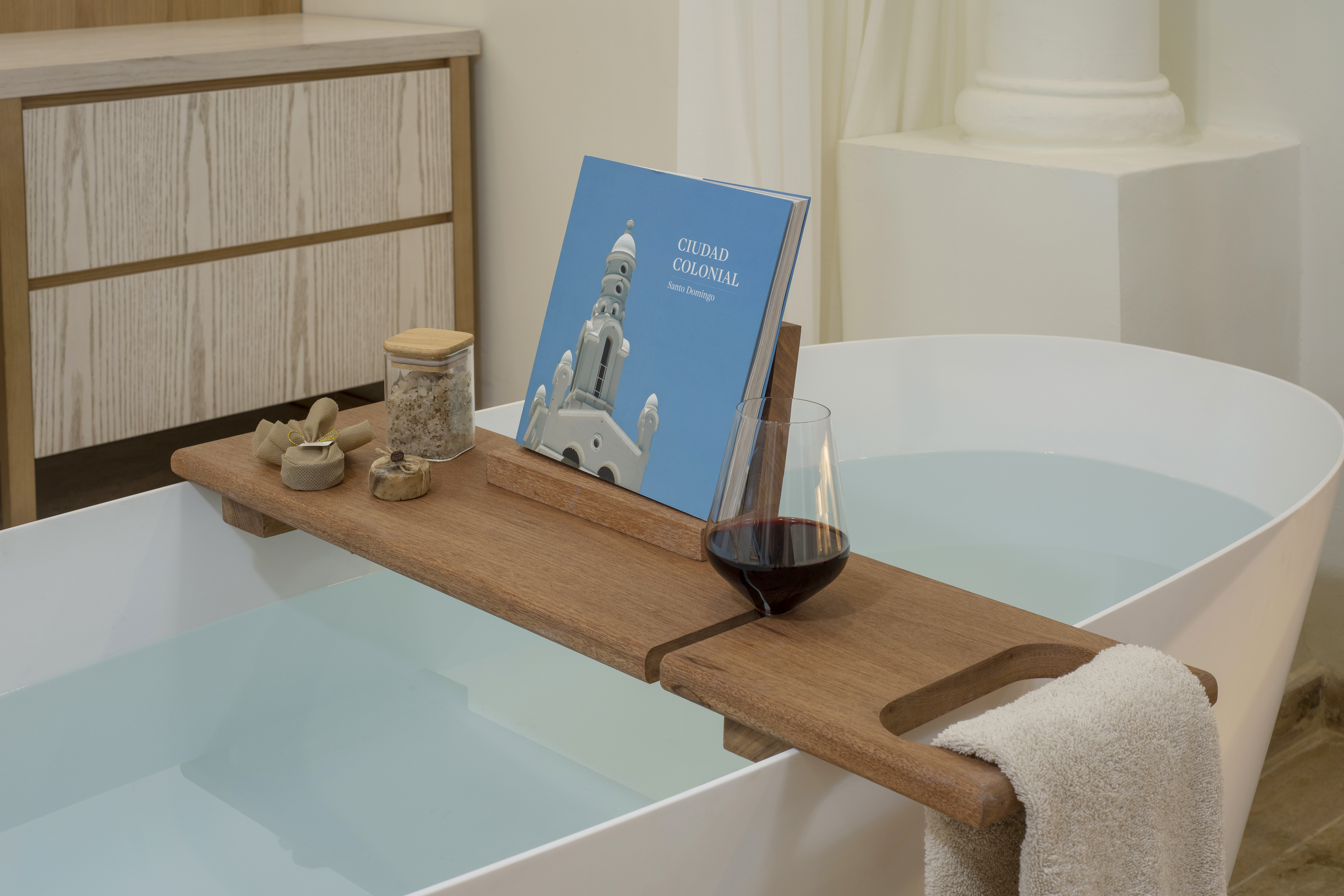 Bathtub with wooden caddy, "Ciudad Colonial" book, red wine, and bath salts.