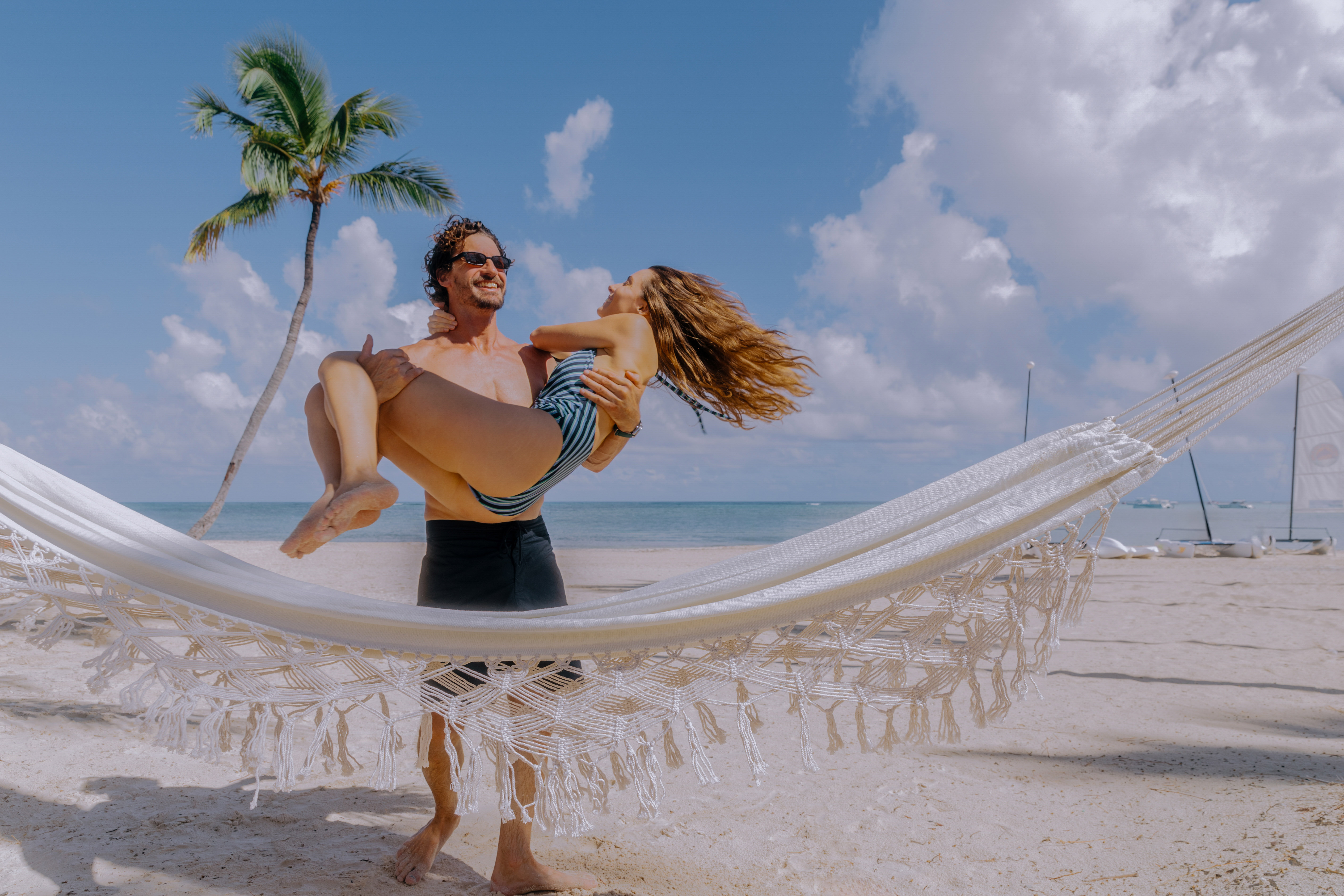 a man holding a woman in a hammock on a beach