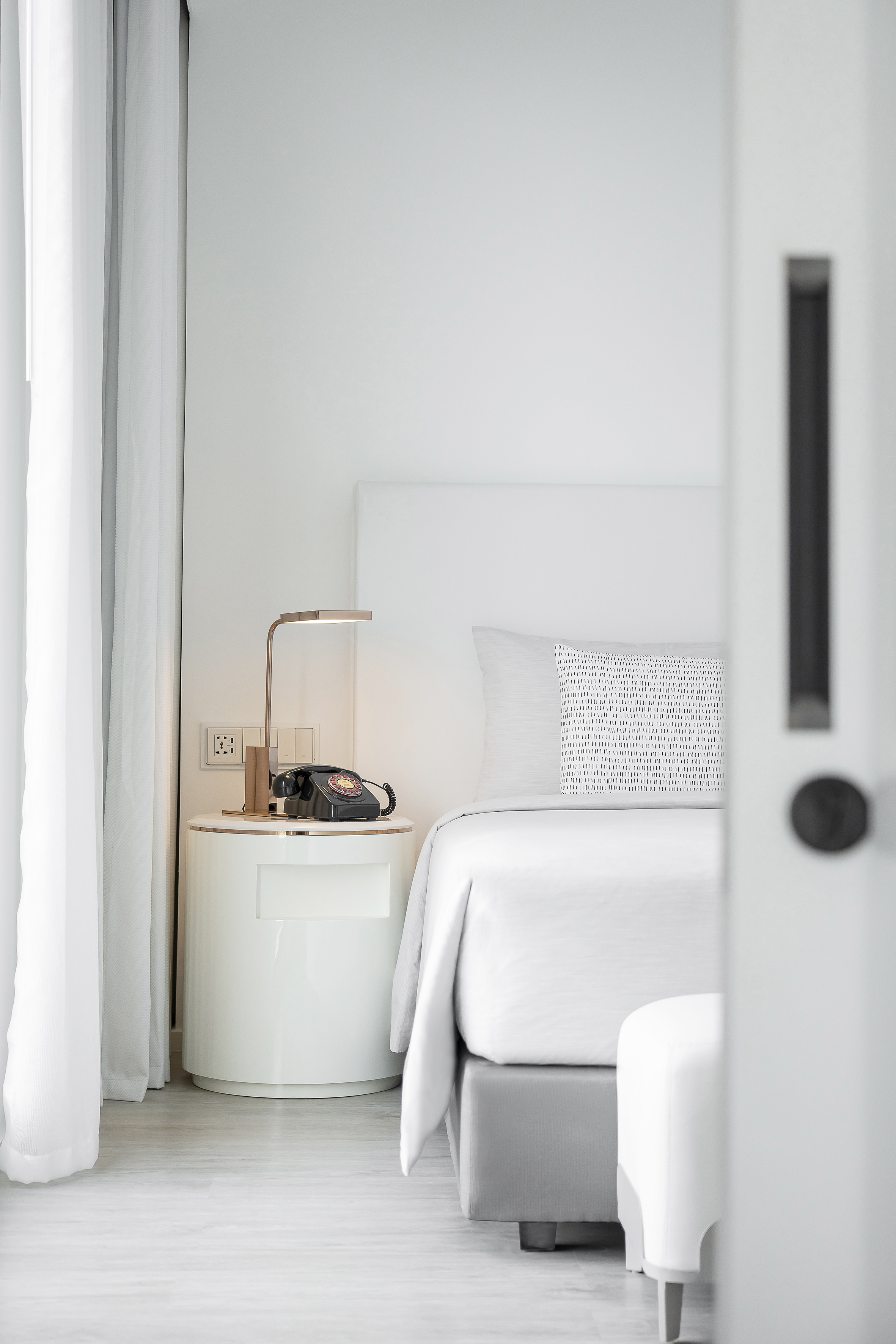 Minimalist white hotel bedroom with nightstand, lamp, and vintage phone.