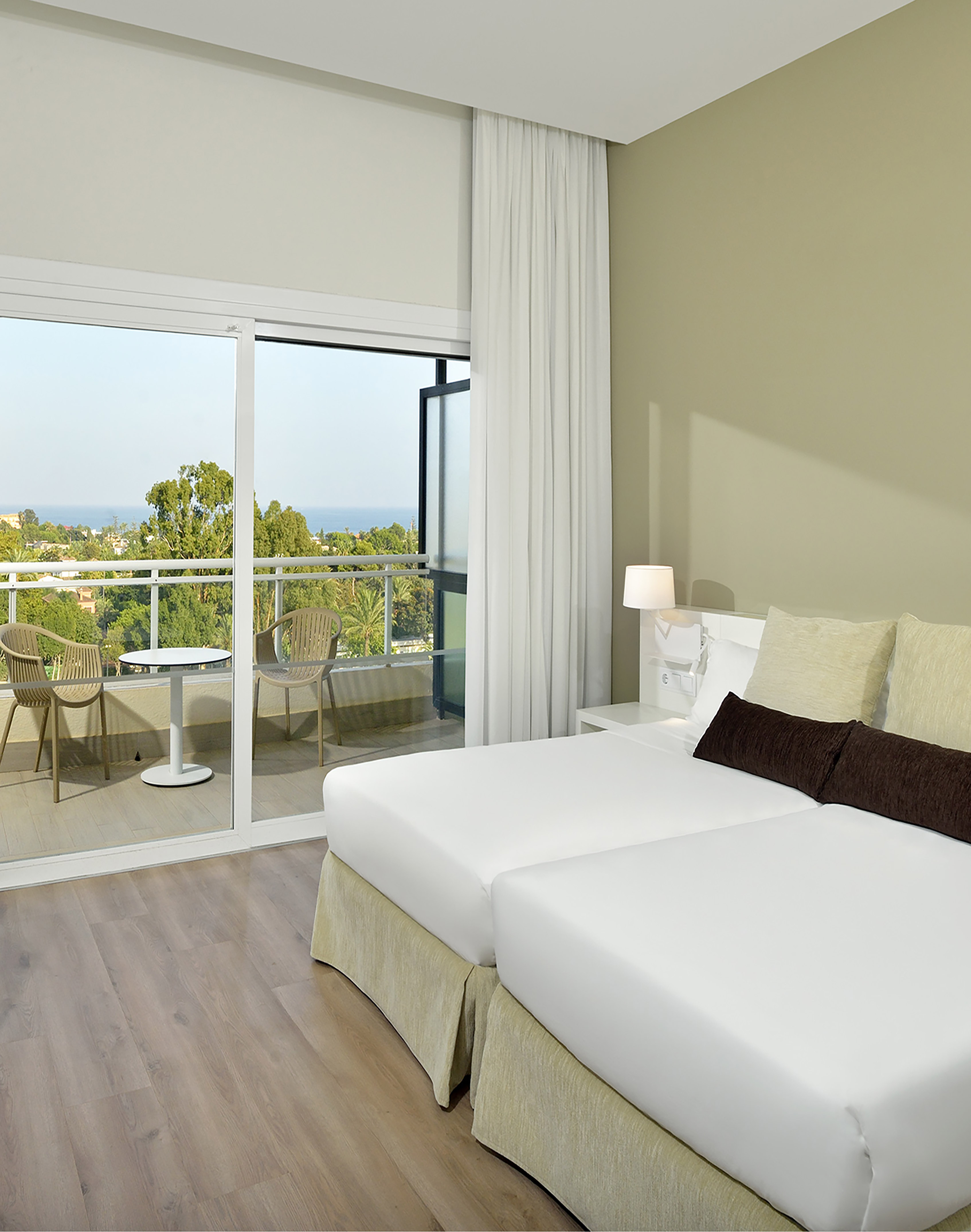 Modern hotel room with twin beds, private balcony, and scenic sea view.