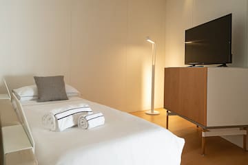 a bed with white sheets and towels on it next to a tv