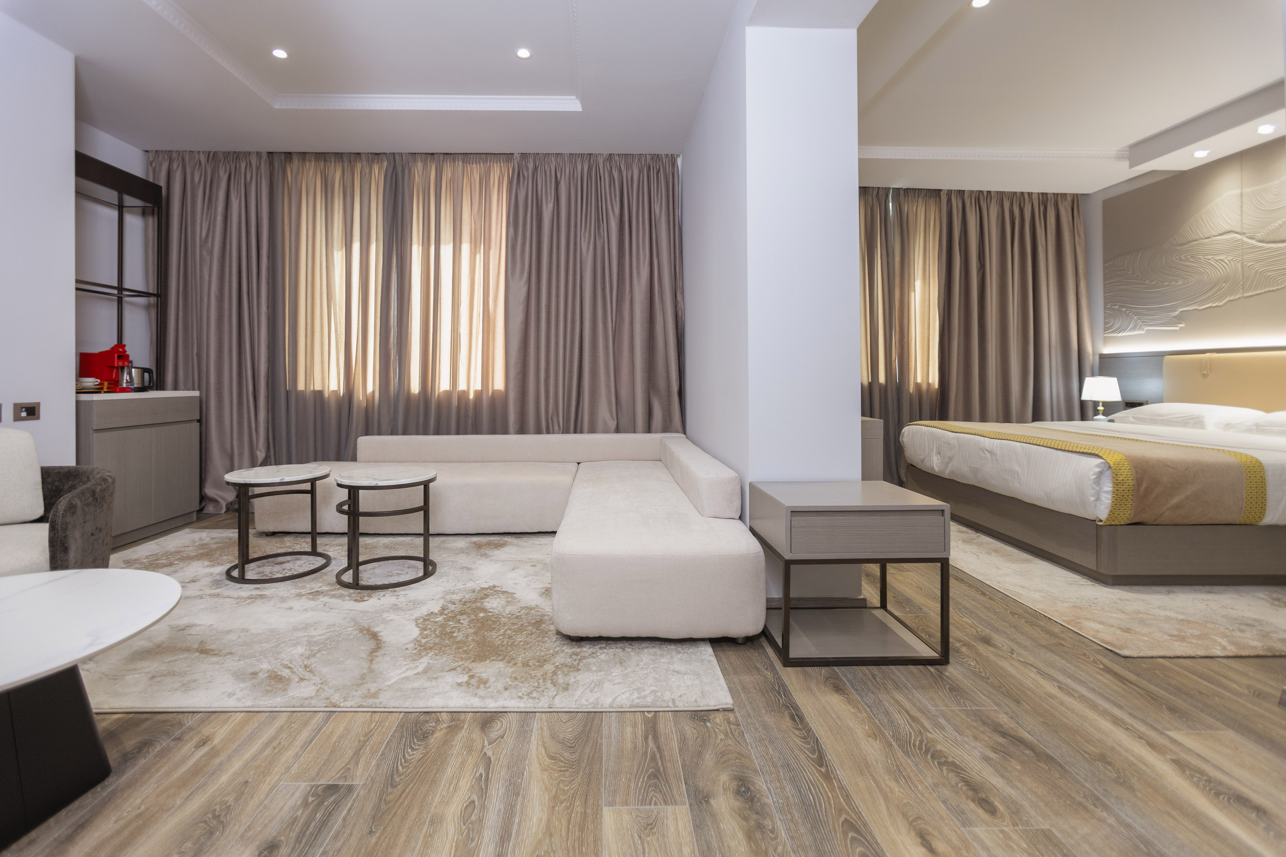 Modern hotel suite living room with sofa, coffee tables, and adjacent bedroom.