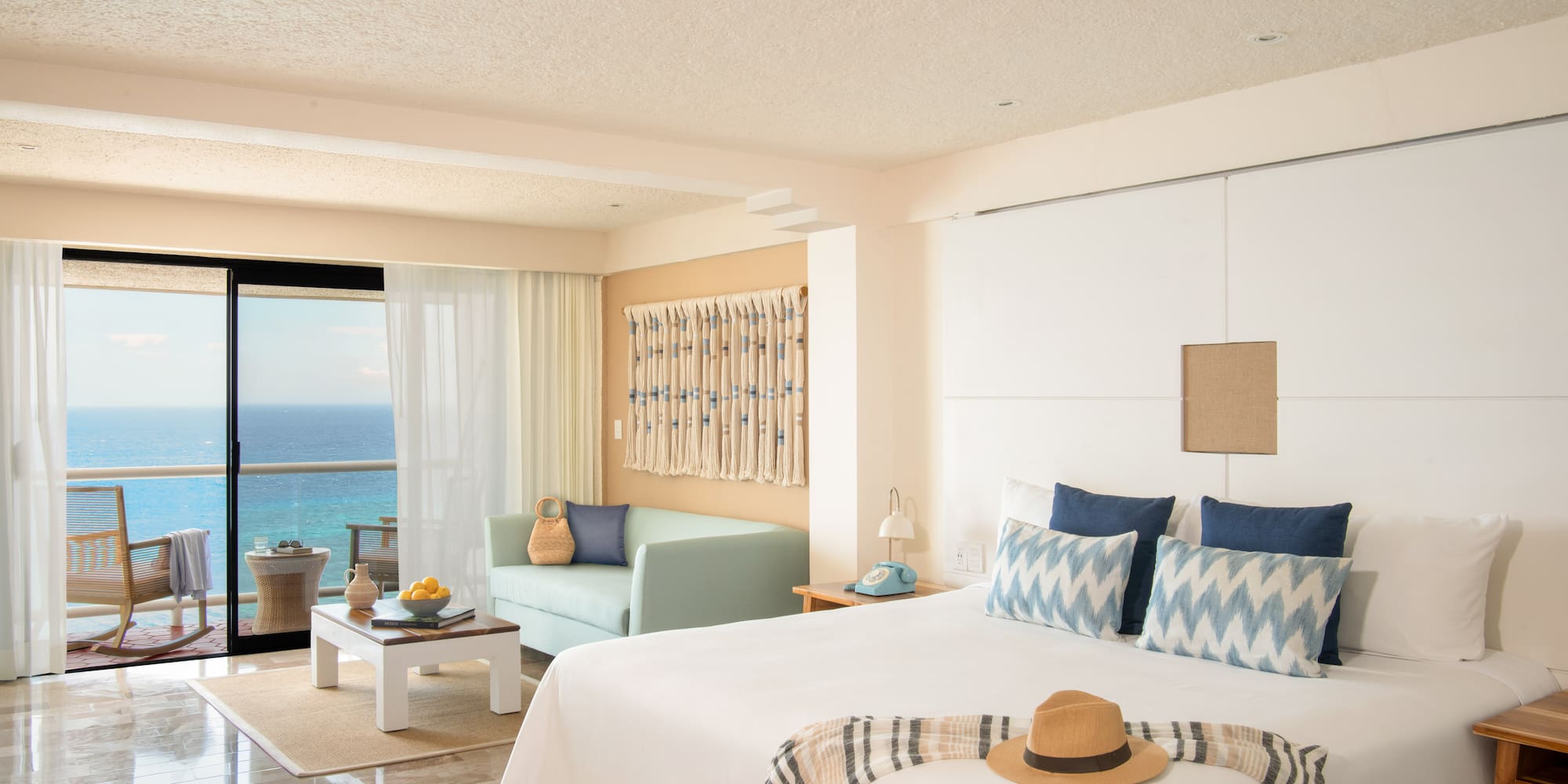 Oceanfront hotel room with balcony, king bed, sofa, and tropical resort decor.