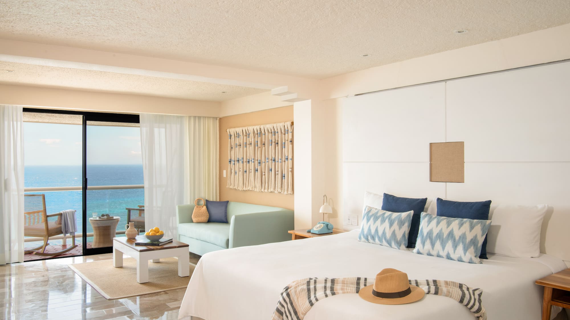 Oceanfront hotel room with balcony, king bed, sofa, and tropical resort decor.