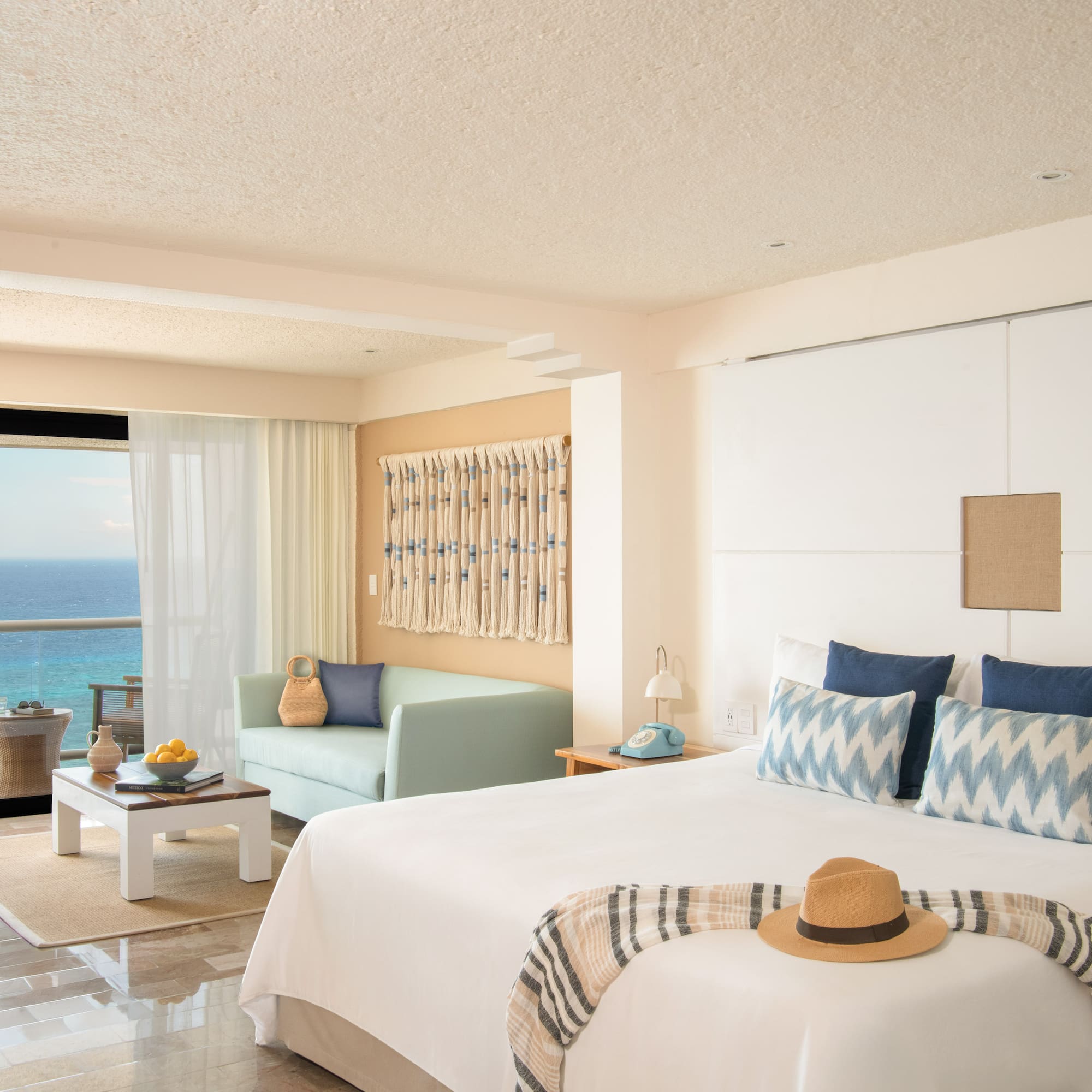 Oceanfront hotel room with balcony, king bed, sofa, and tropical resort decor.