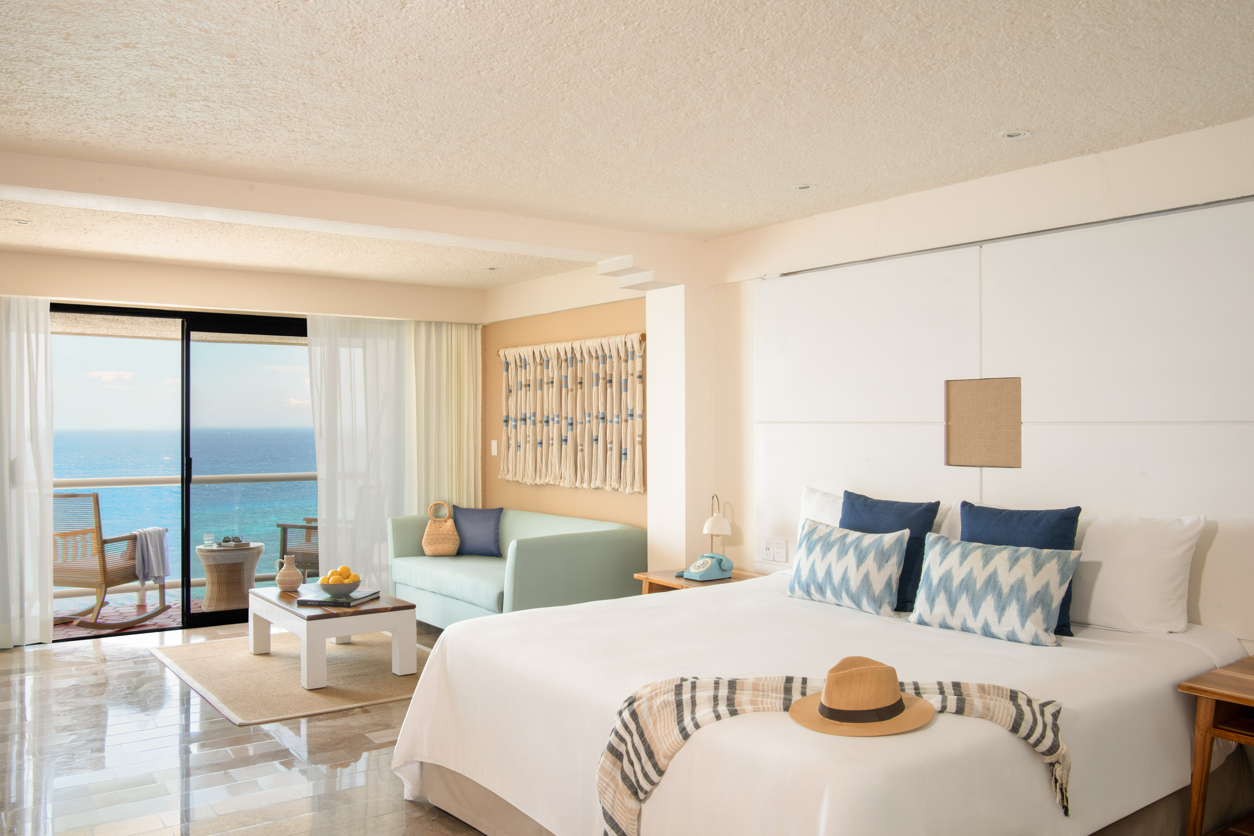 Oceanfront hotel room with balcony, king bed, sofa, and tropical resort decor.
