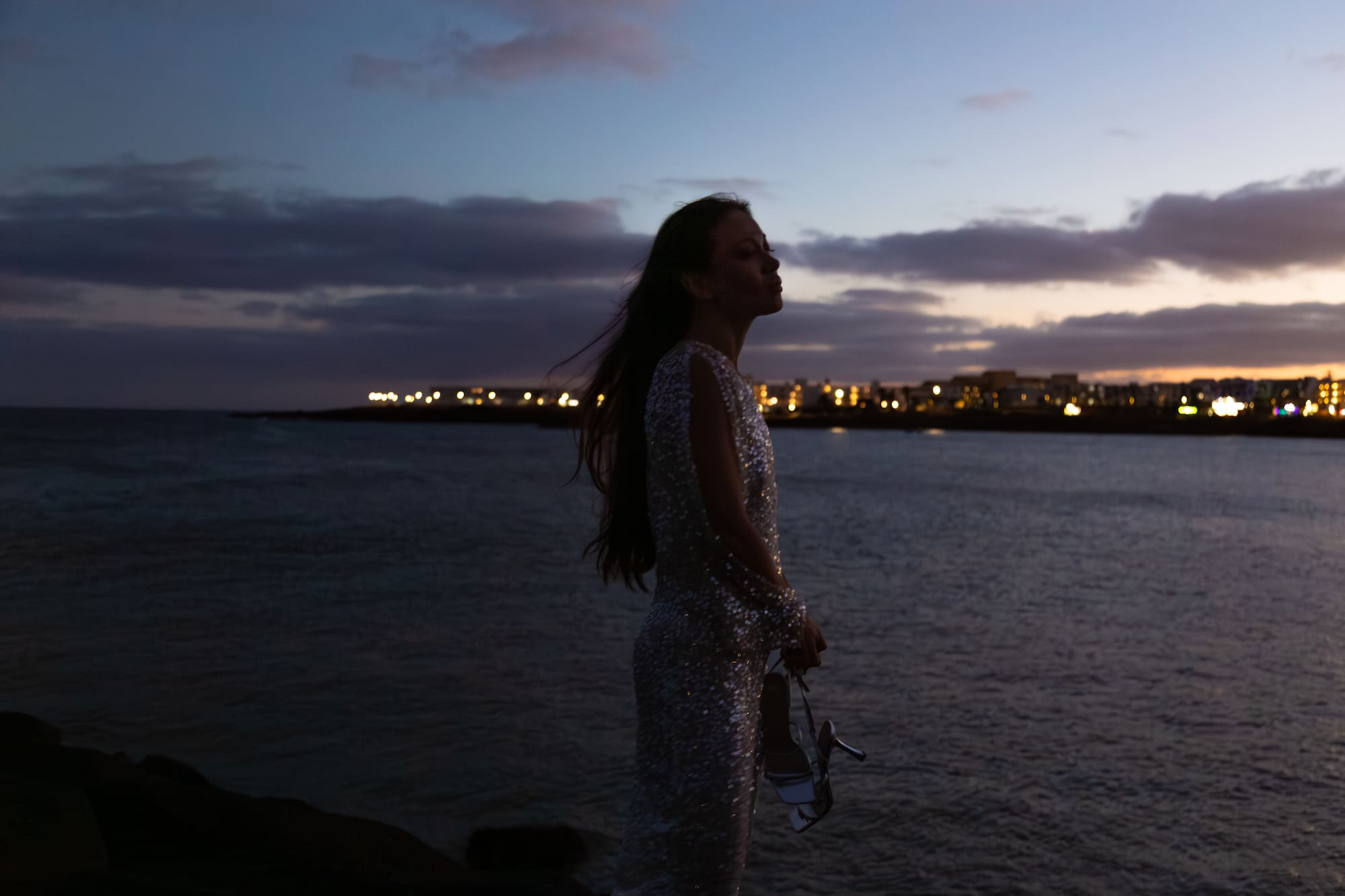 a woman standing on a rock by water with a city in the background
