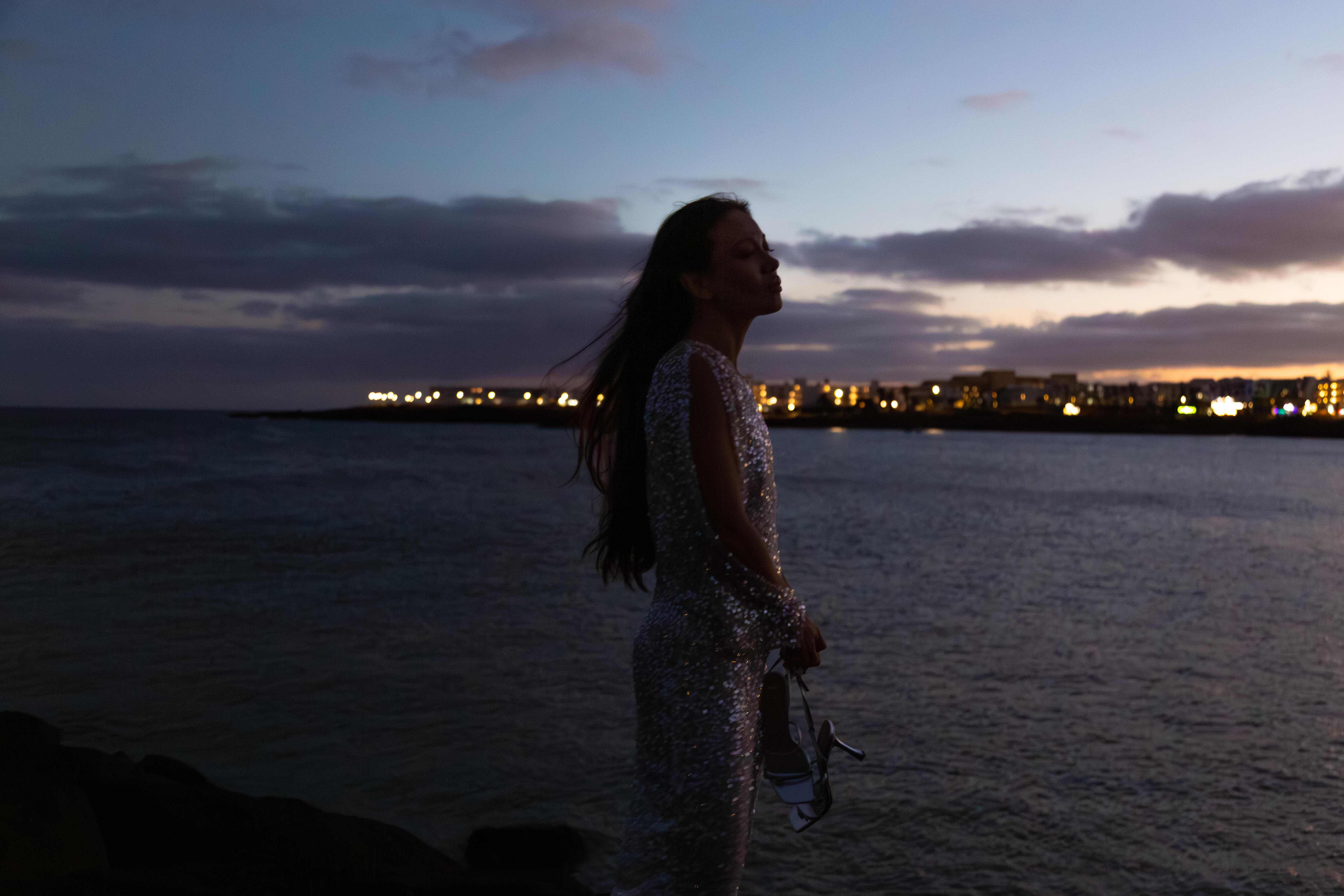 a woman standing on a rock by water with a city in the background