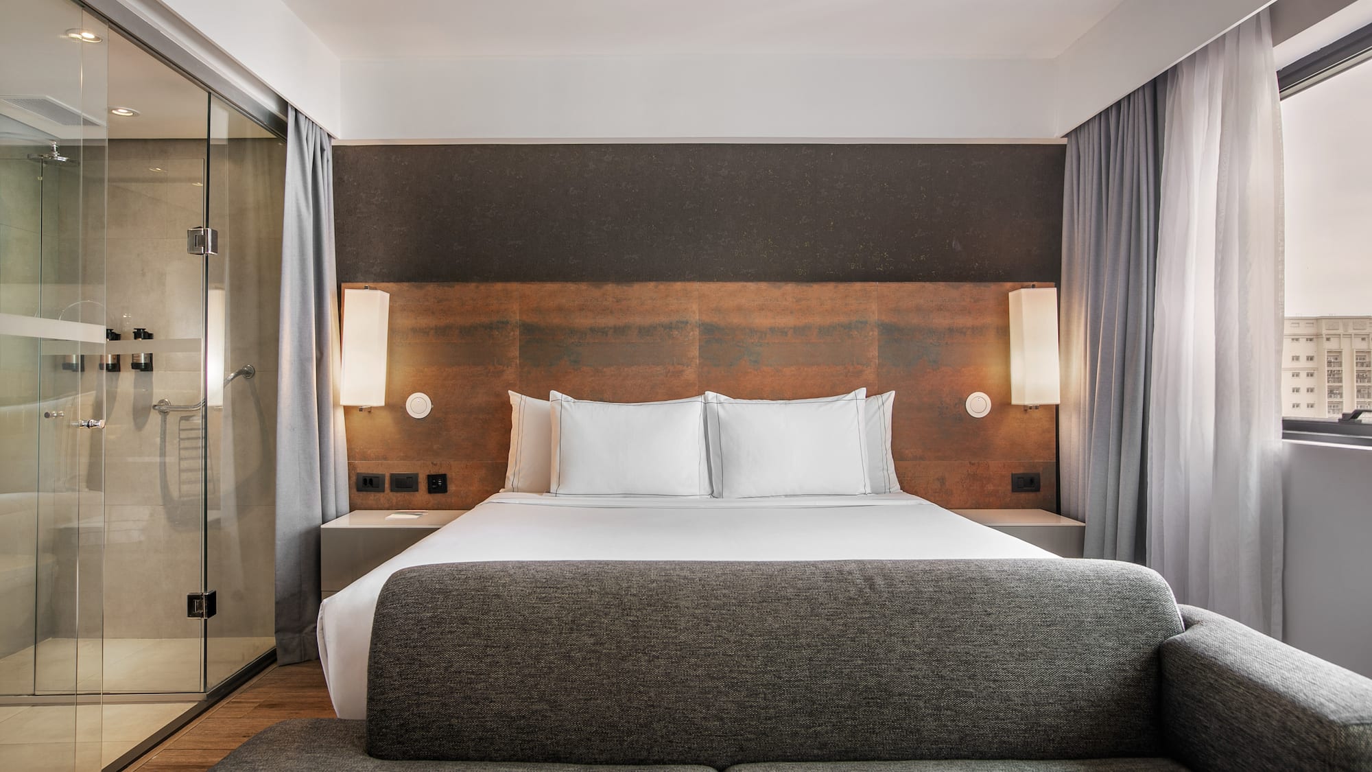 Quarto de hotel moderno com cama grande, cabeceira de madeira, banheiro de vidro e sofá cinza. - Grand Premium - Meliá Ibirapuera, São Paulo