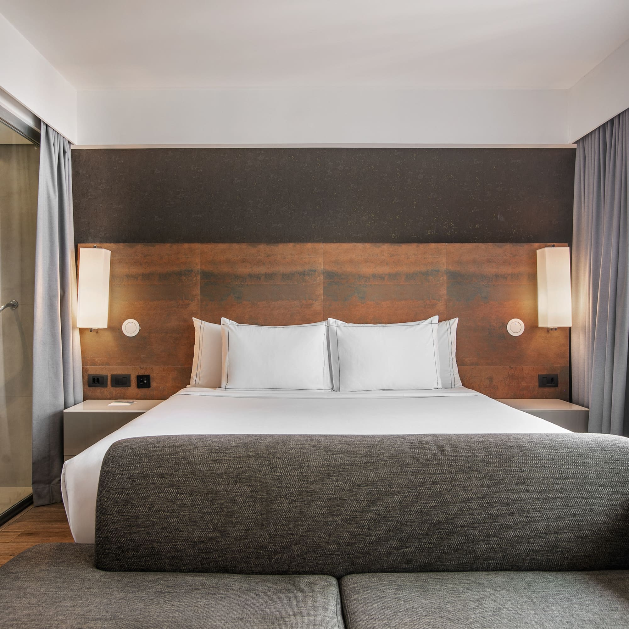 Quarto de hotel moderno com cama grande, cabeceira de madeira, banheiro de vidro e sofá cinza. - Grand Premium - Meliá Ibirapuera, São Paulo