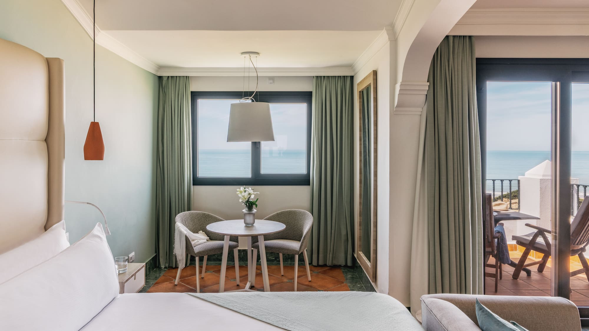 Luxury hotel room with ocean view balcony, king bed, and modern seating area.