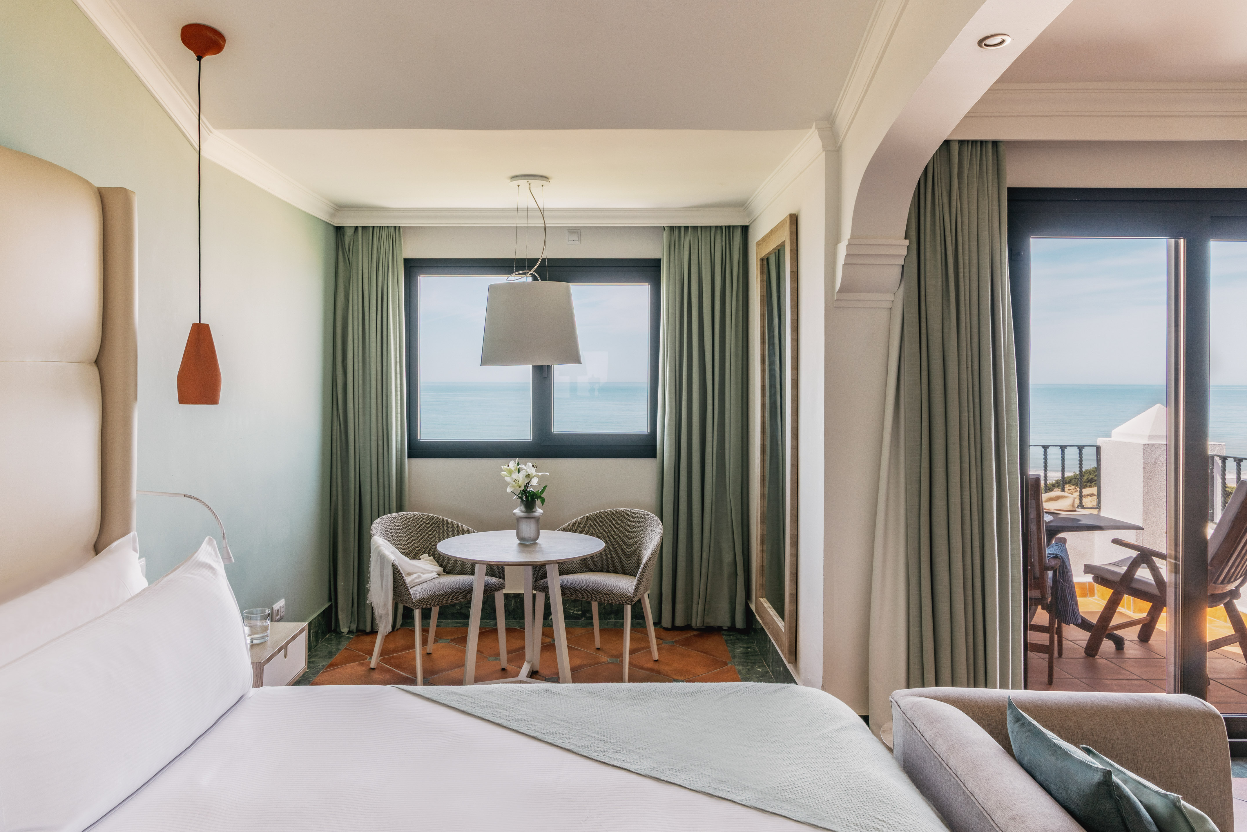 Luxury hotel room with ocean view balcony, king bed, and modern seating area.