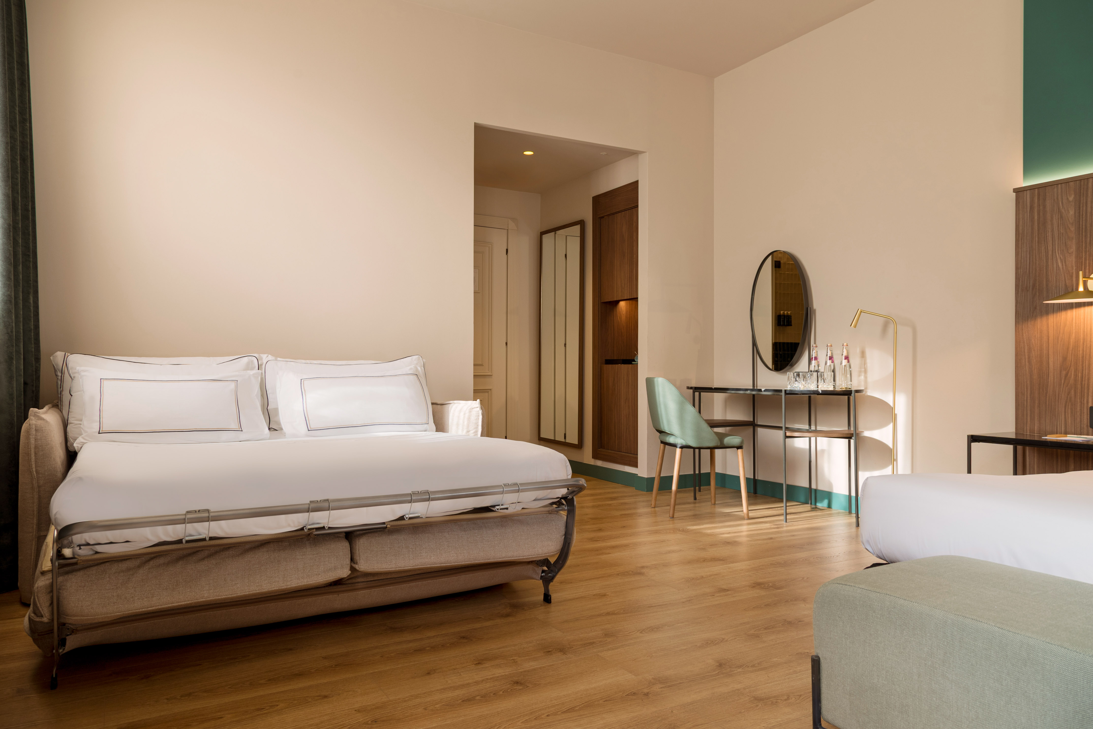 Cozy hotel room with sofa bed, wooden floor, and modern vanity.