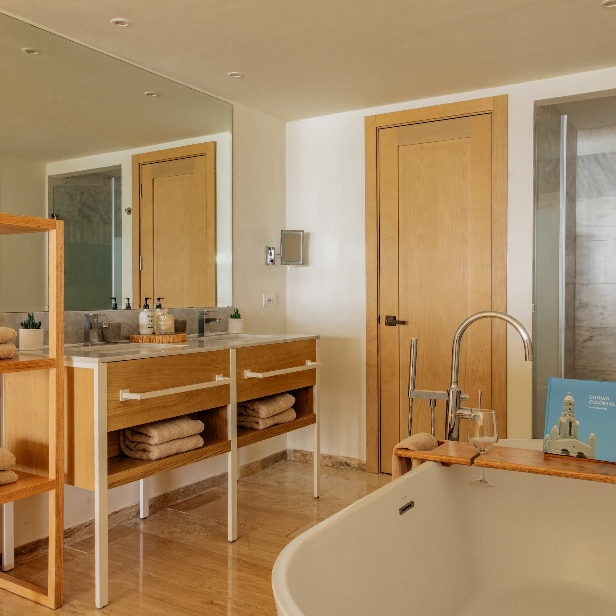 Modern hotel bathroom with white tub, wooden vanity, and marble shower.