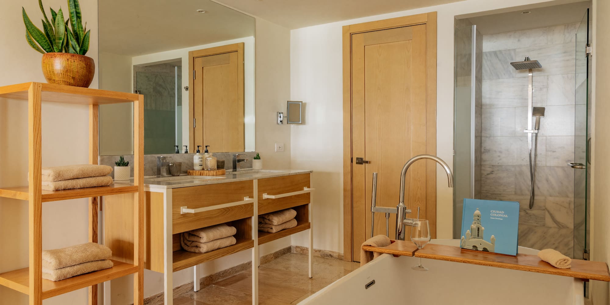 Modern hotel bathroom with white tub, wooden vanity, and marble shower.