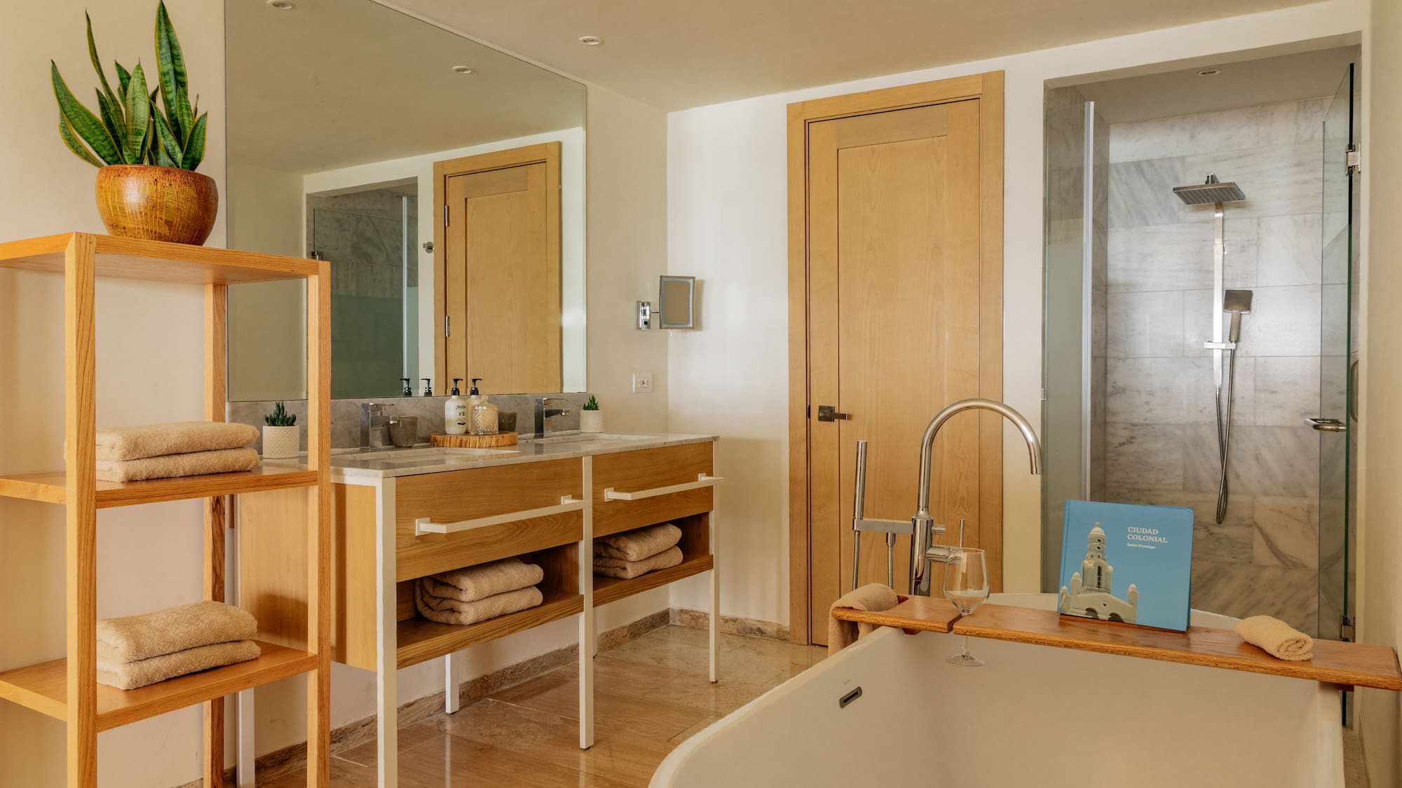 Modern hotel bathroom with white tub, wooden vanity, and marble shower.