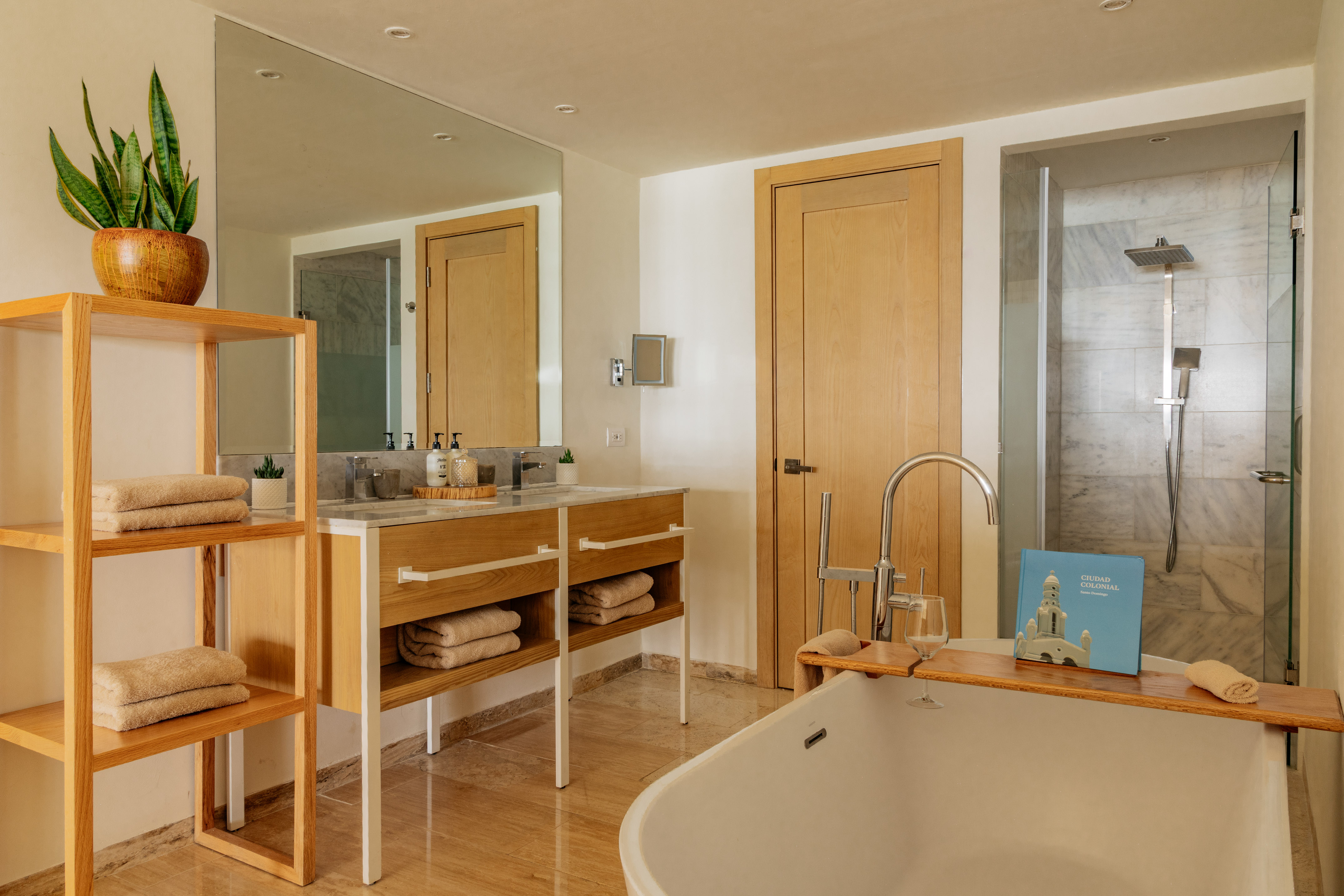 Modern hotel bathroom with white tub, wooden vanity, and marble shower.