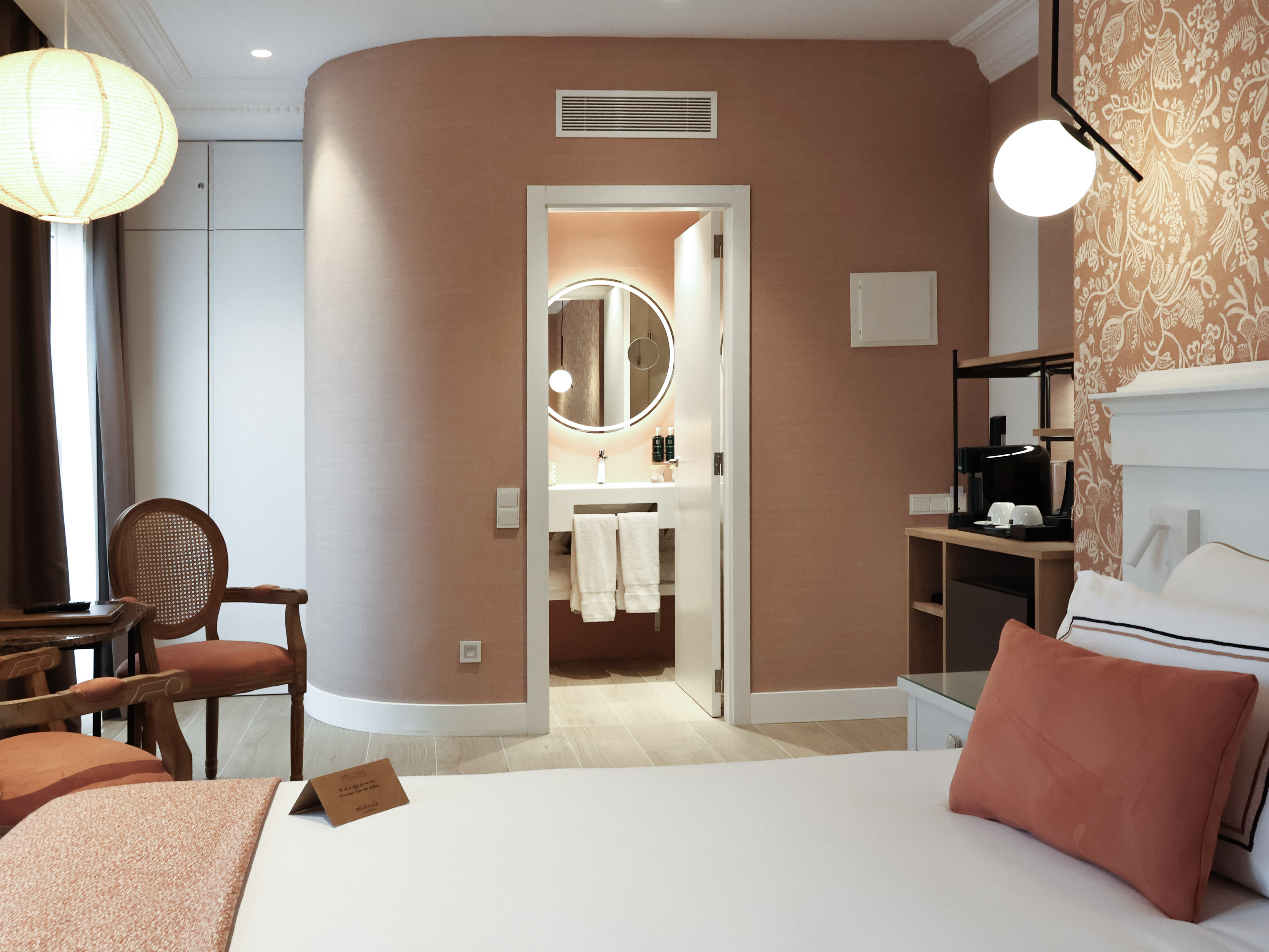 Modern hotel room with bed, salmon walls, and view into ensuite bathroom.