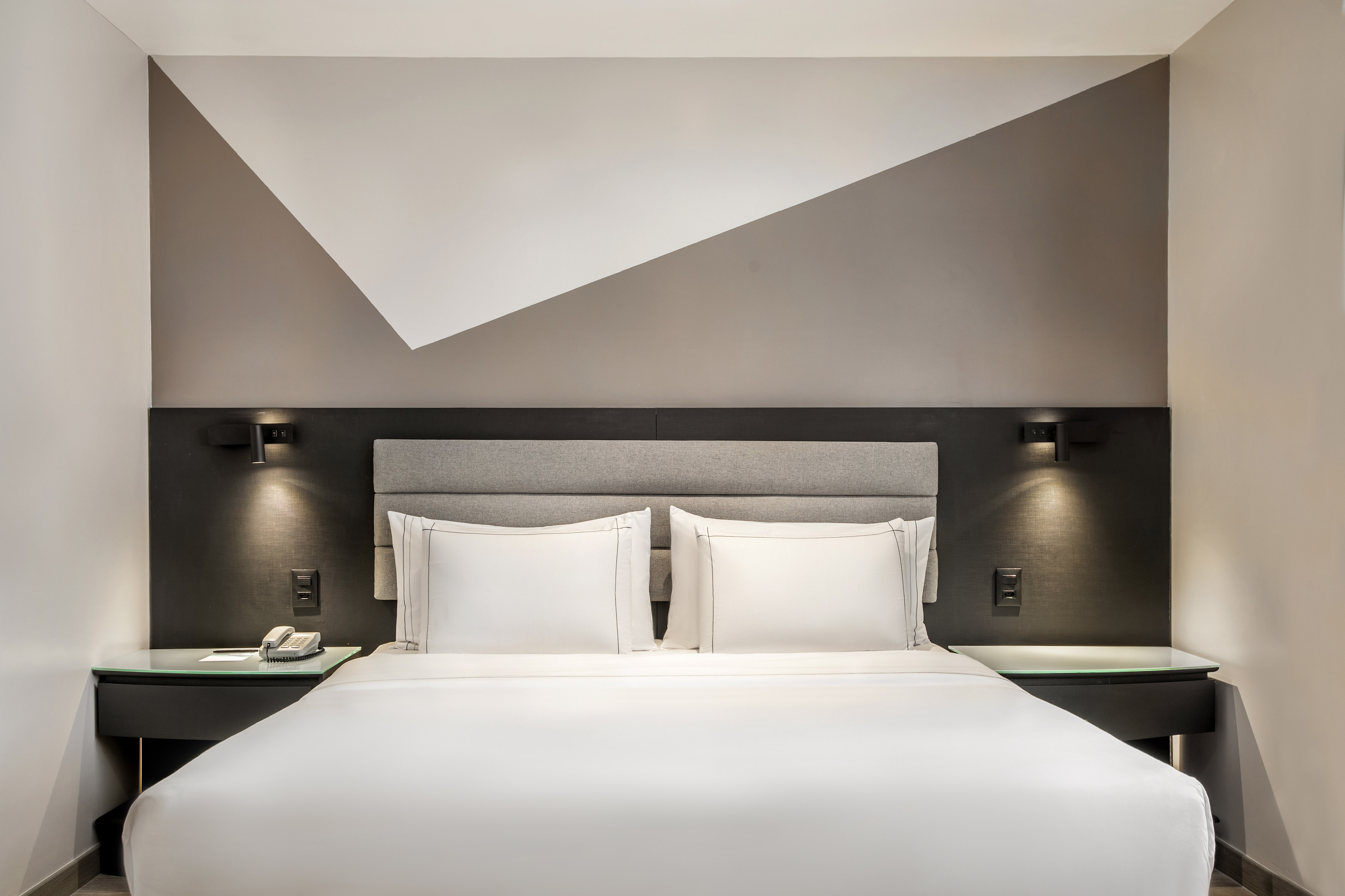 Hotel room with white bed, grey headboard, and modern geometric accent wall.