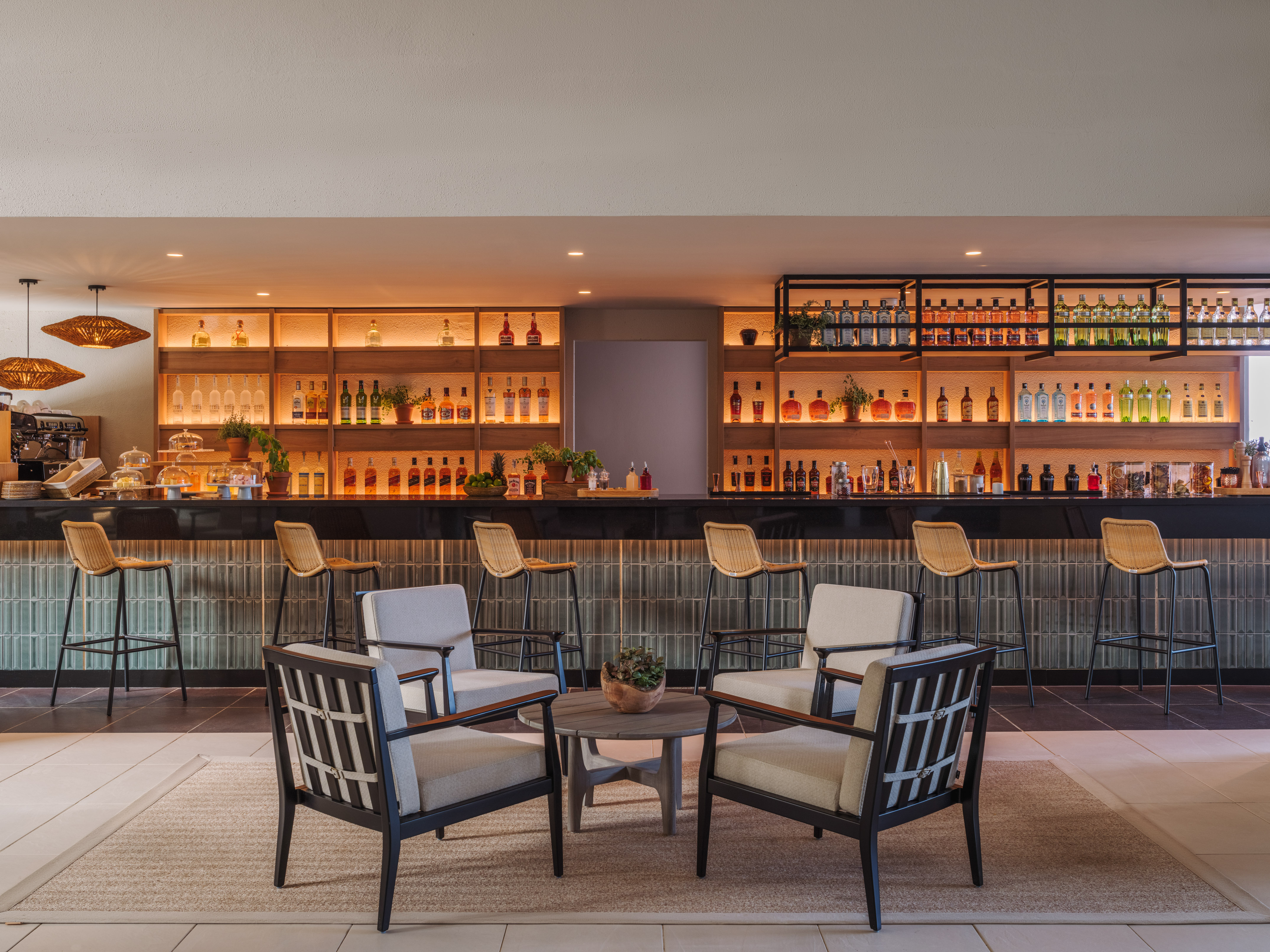 Modern hotel bar with backlit liquor shelves, wicker barstools, and lounge chairs.