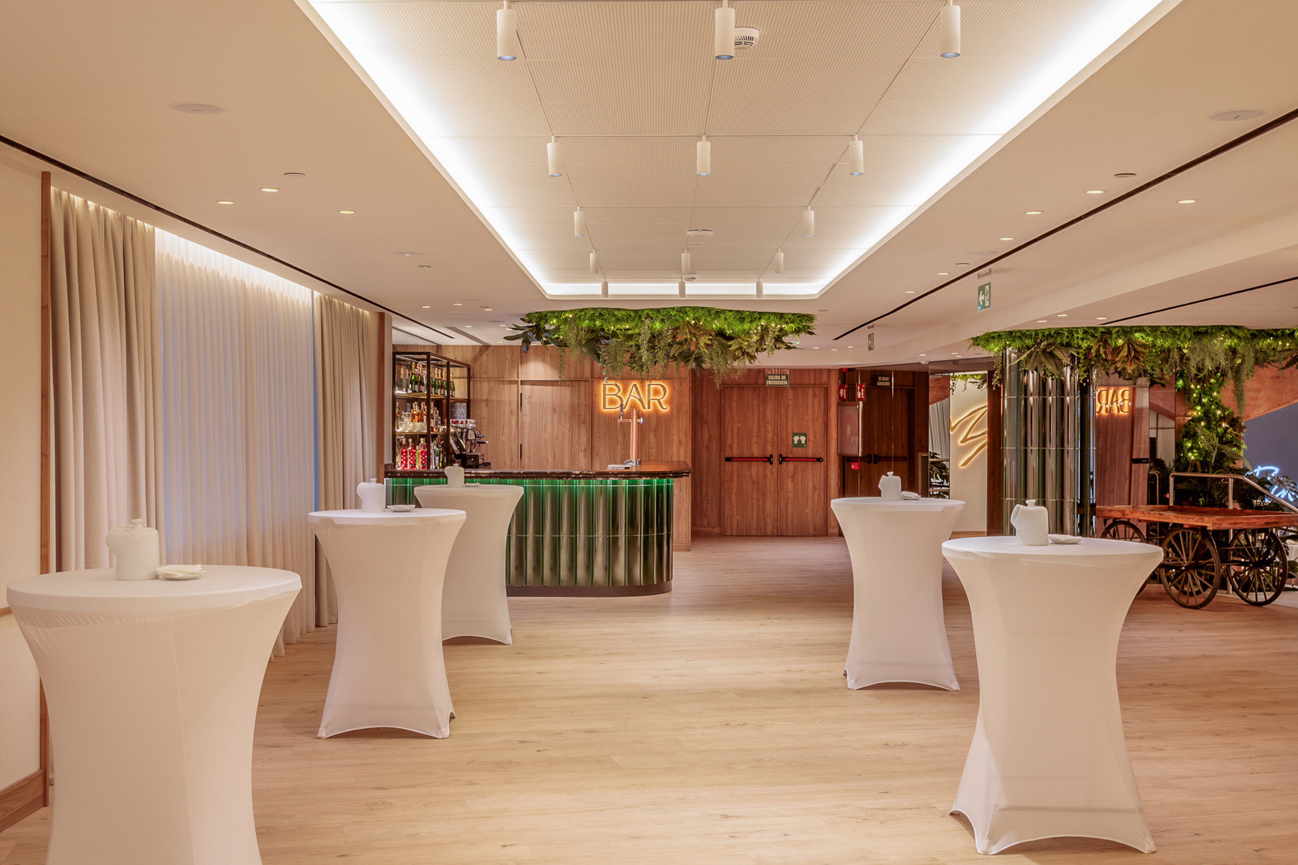 Modern event bar with cocktail tables, neon BAR sign, and hanging greenery.