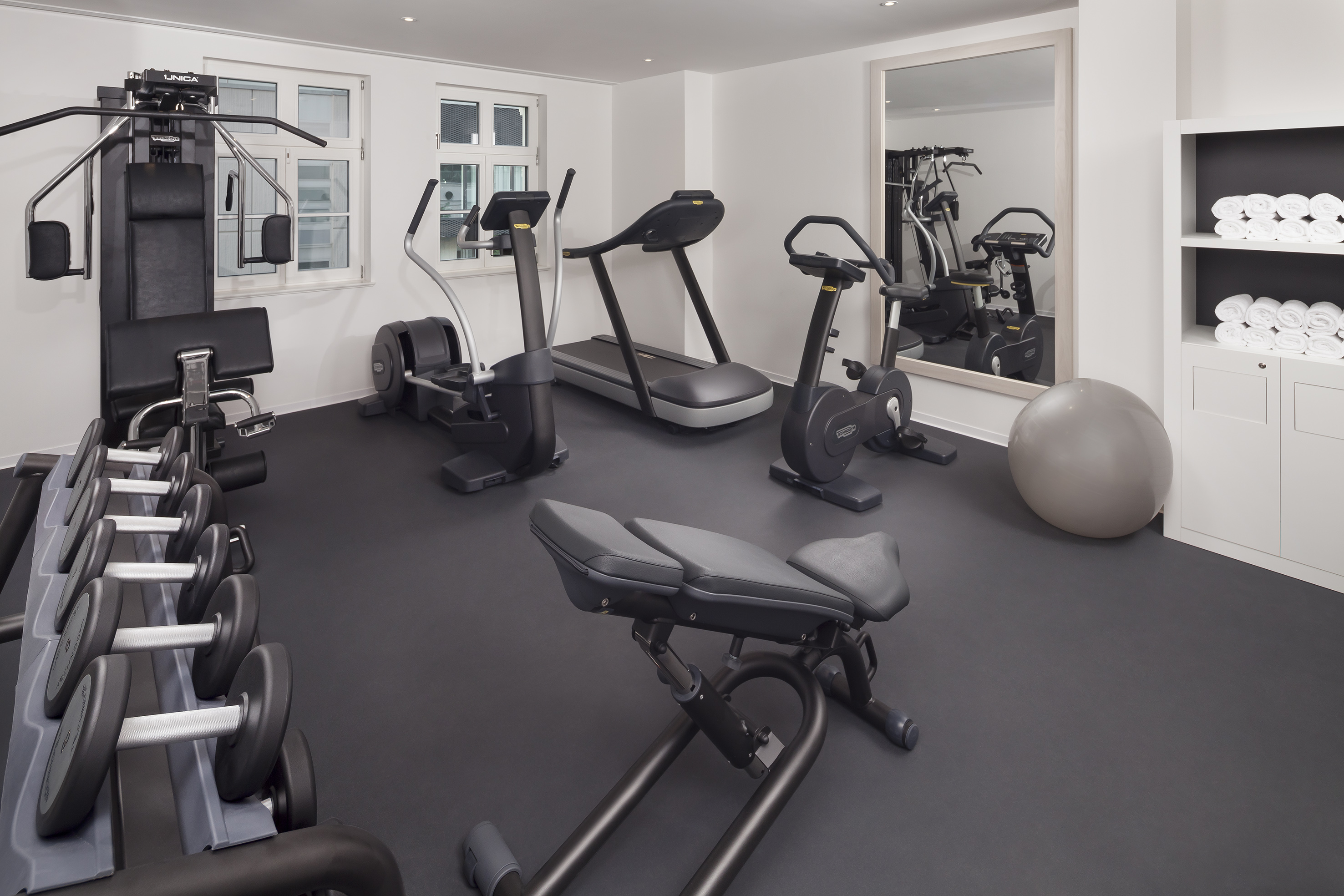 Modern gym with treadmill, elliptical, weight machine, and free weights.