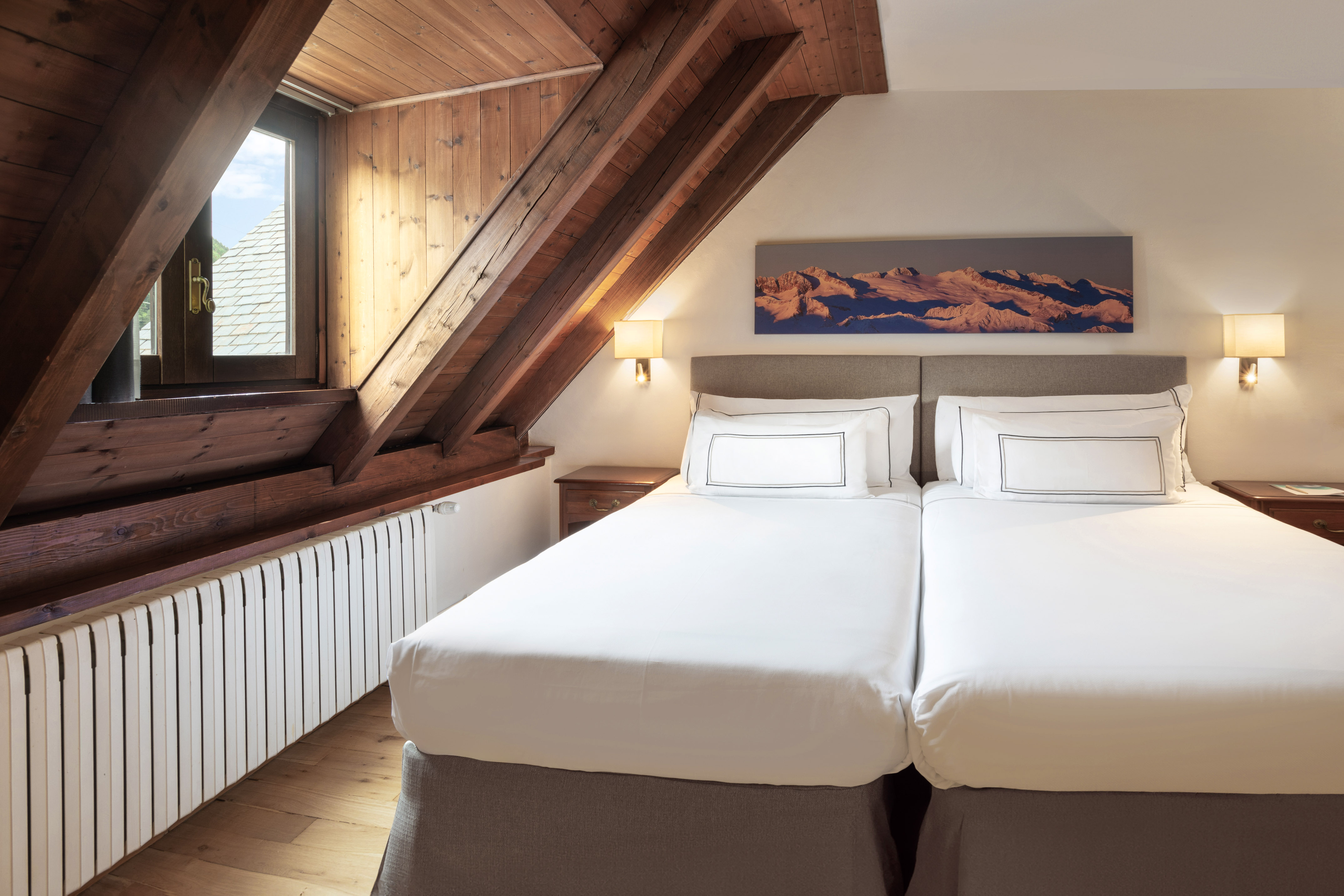 Hotel attic bedroom with twin beds, exposed wooden beams, and mountain wall art.