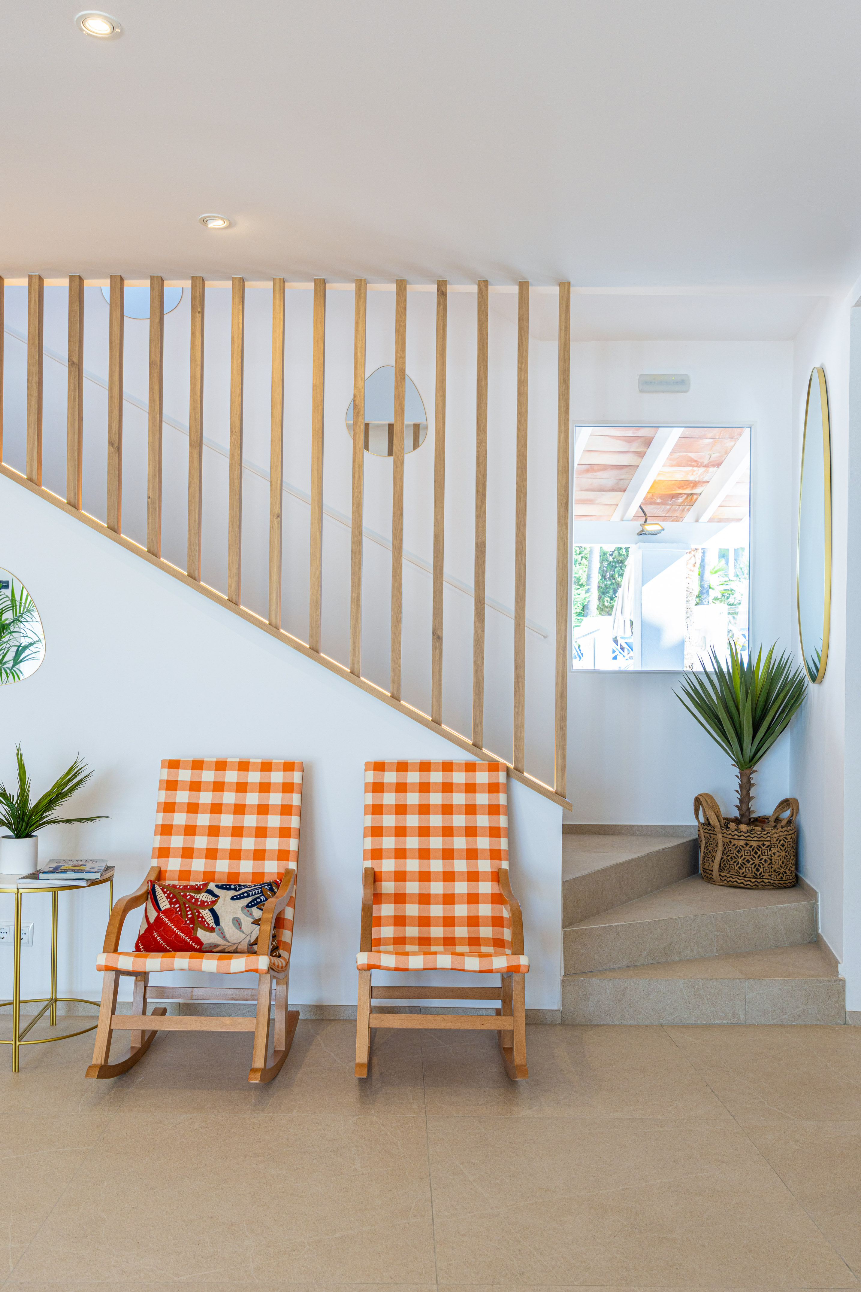 Modern interior with wooden slat staircase, orange checkered chairs, and plants.