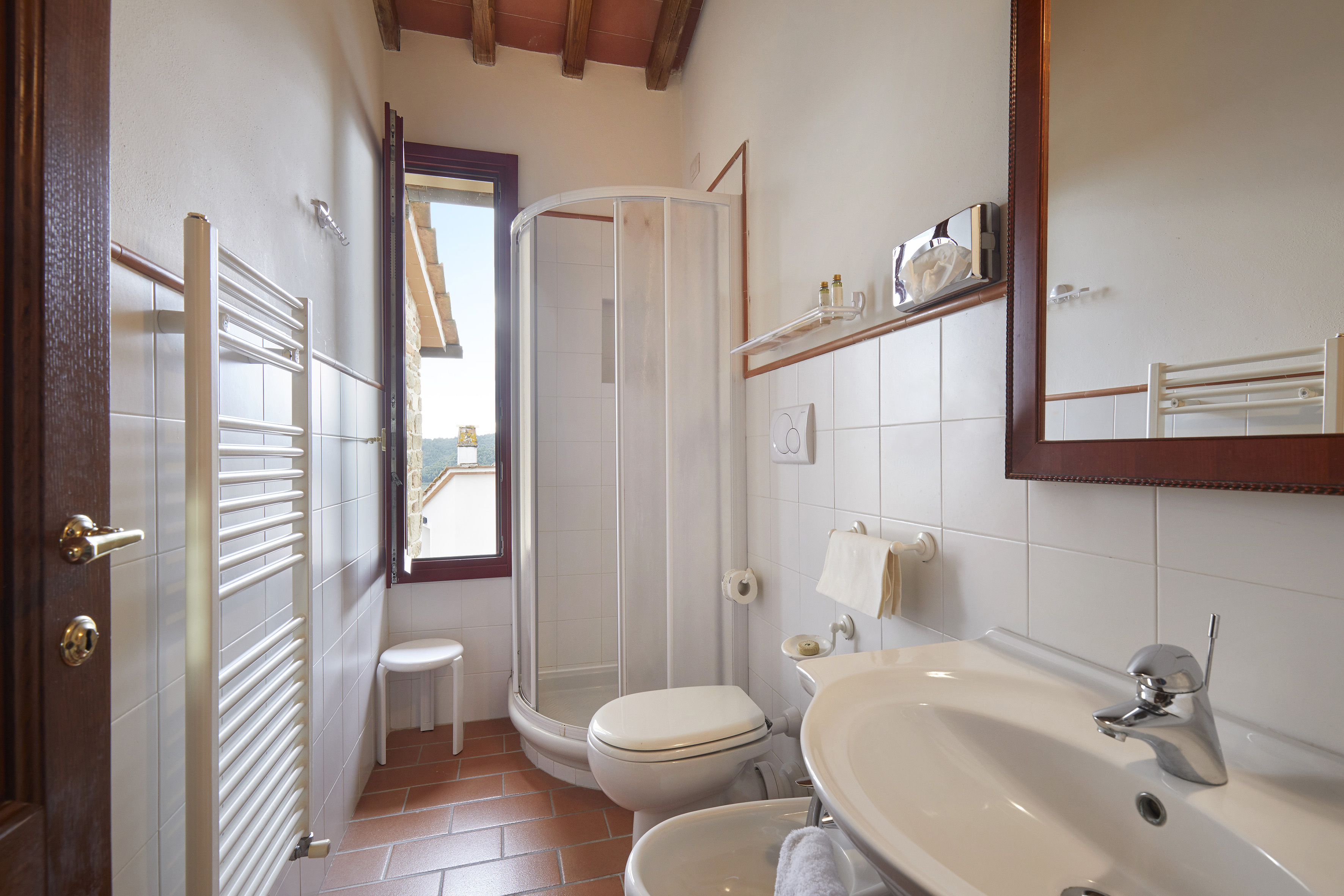 Tiled bathroom with shower, toilet, sink, bidet, terracotta floor, window.