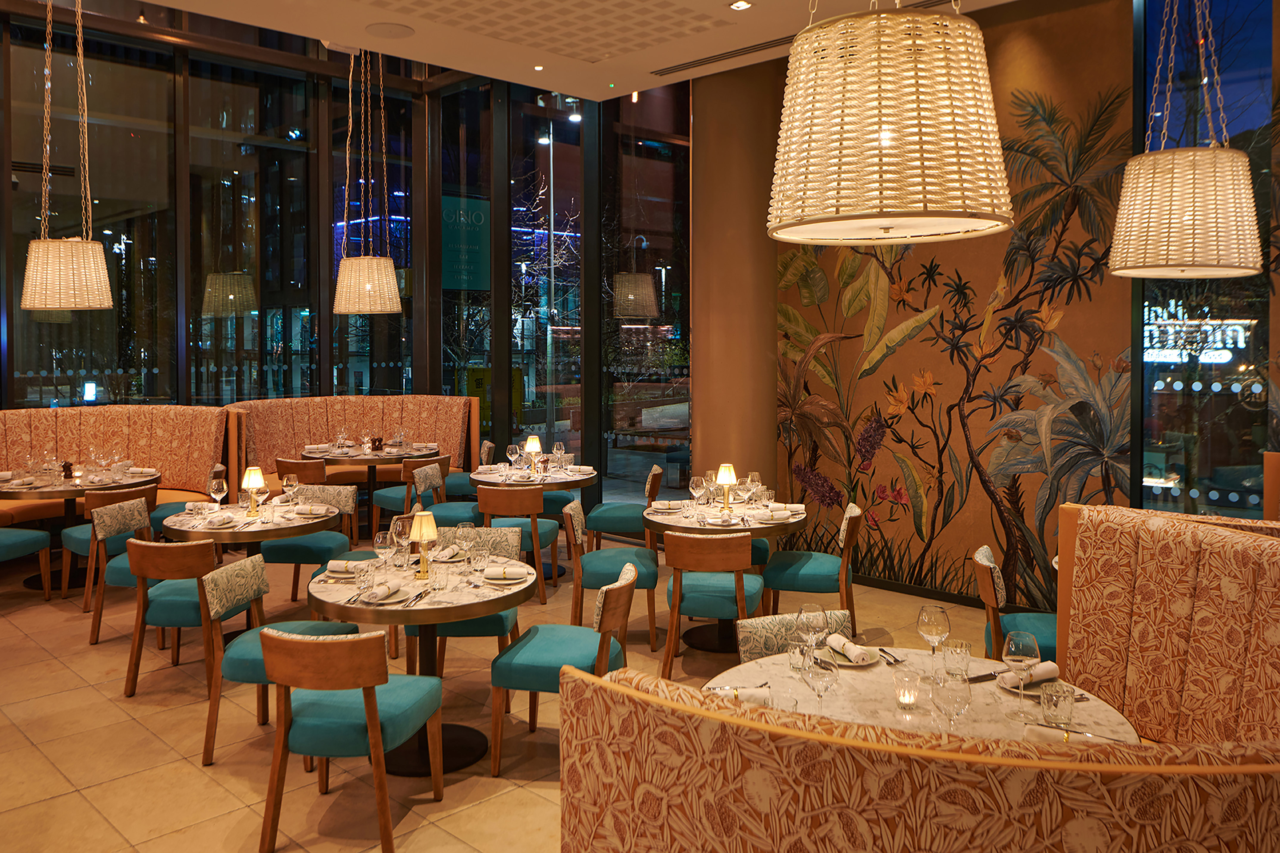 Elegant restaurant dining room with tropical mural, wicker lights, and teal seating.