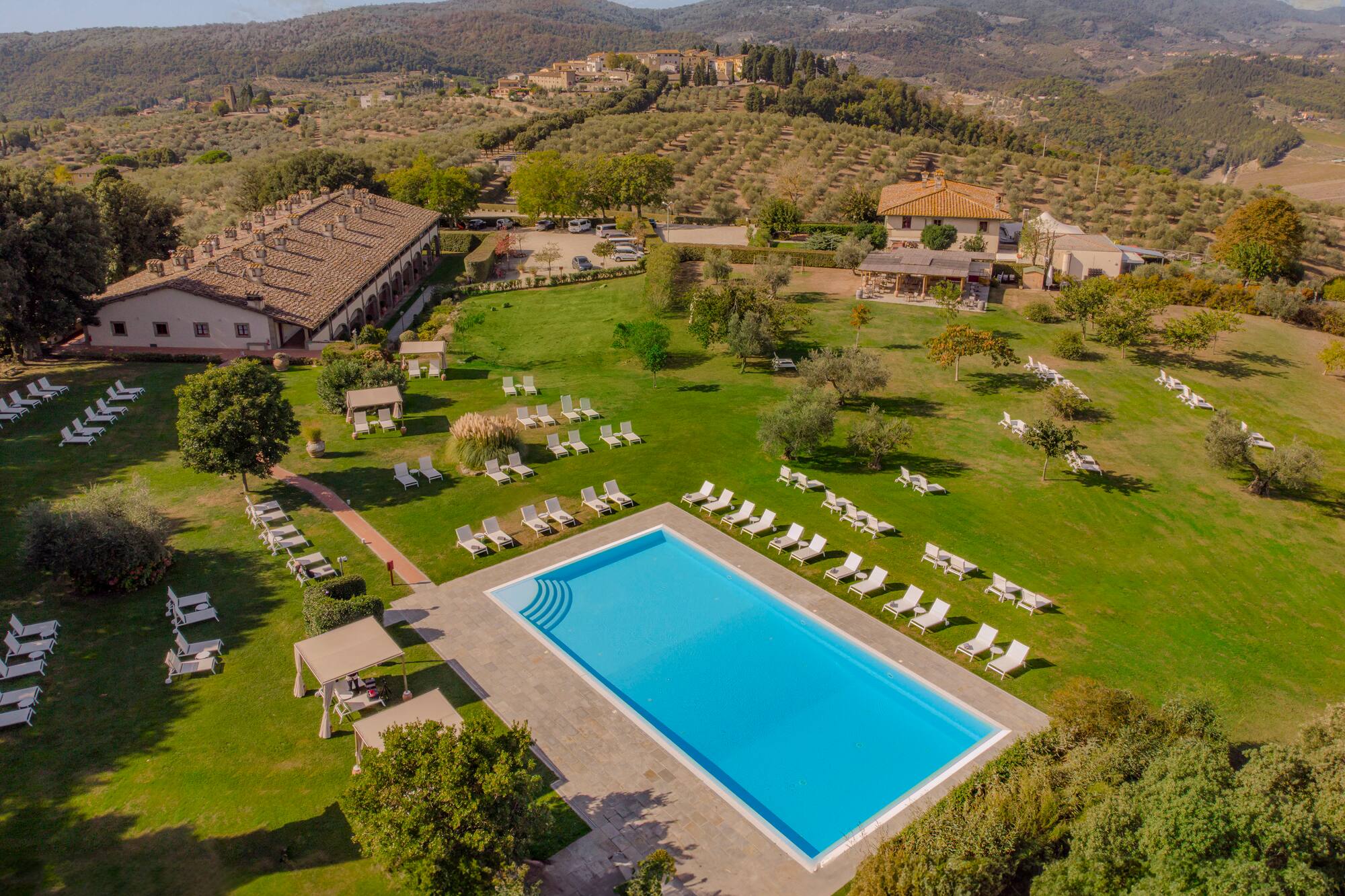 Aerial view of Tuscan resort with large pool, villas, and olive groves.