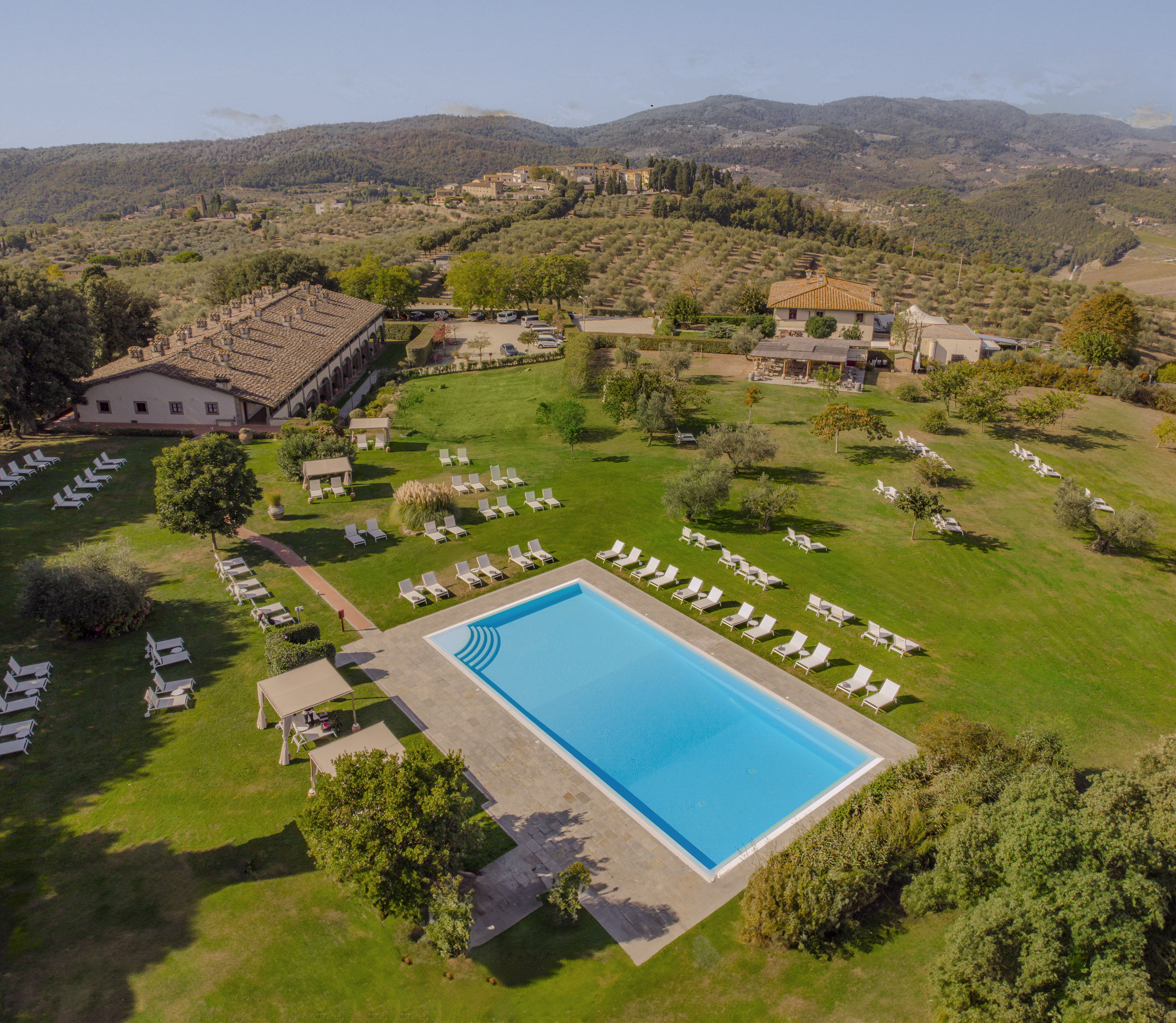 Aerial view of Tuscan resort with large pool, villas, and olive groves.