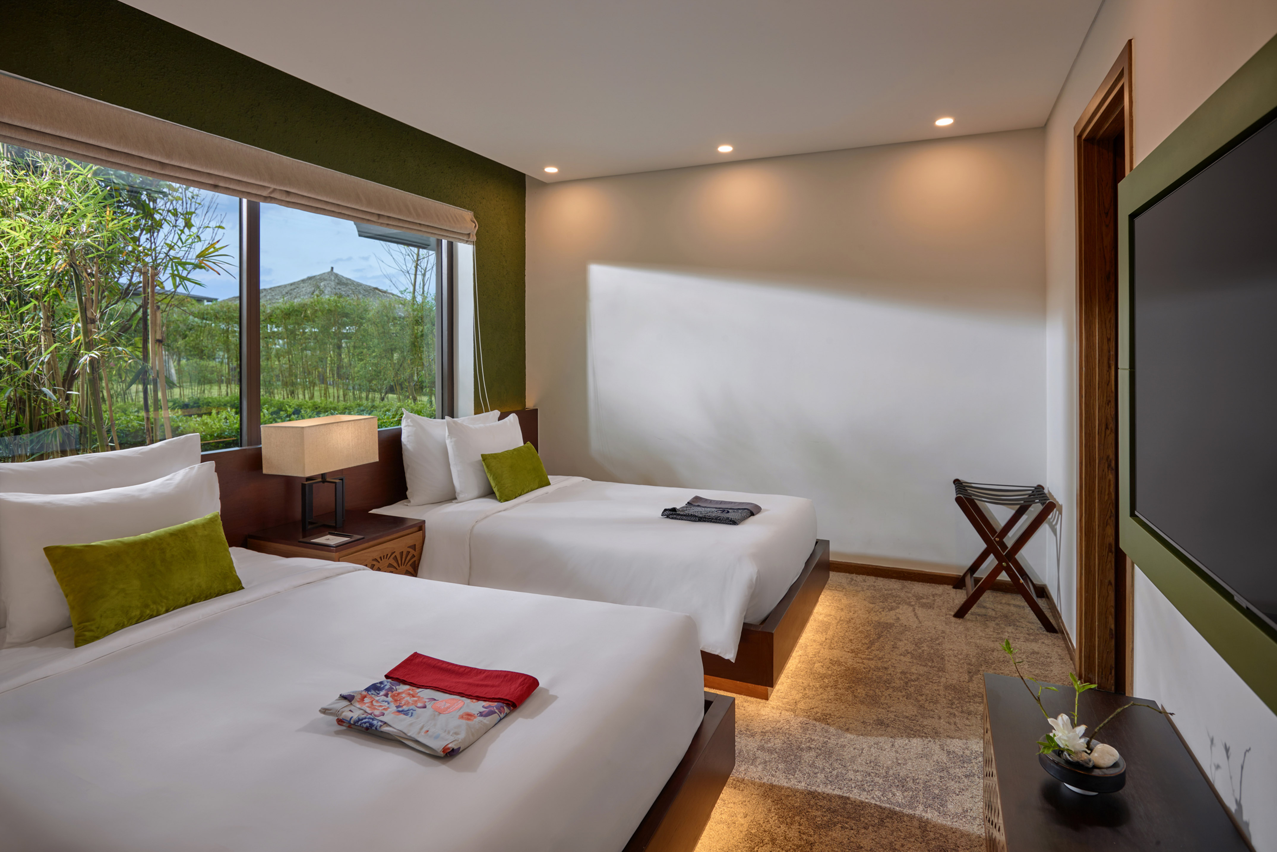 Modern twin hotel room with bamboo garden view from large window.