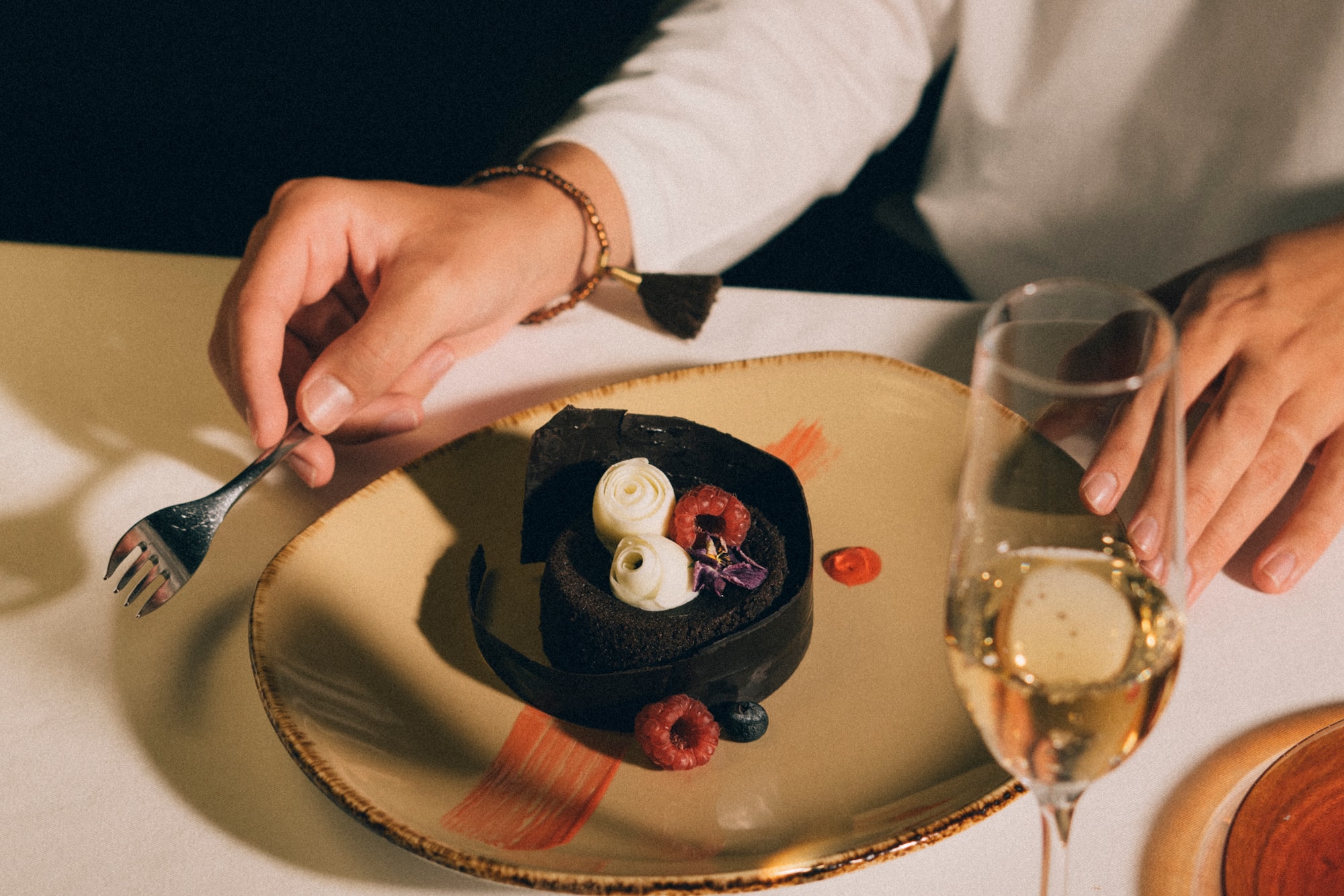 Elegant chocolate dessert with berries and cream, person with fork and champagne.