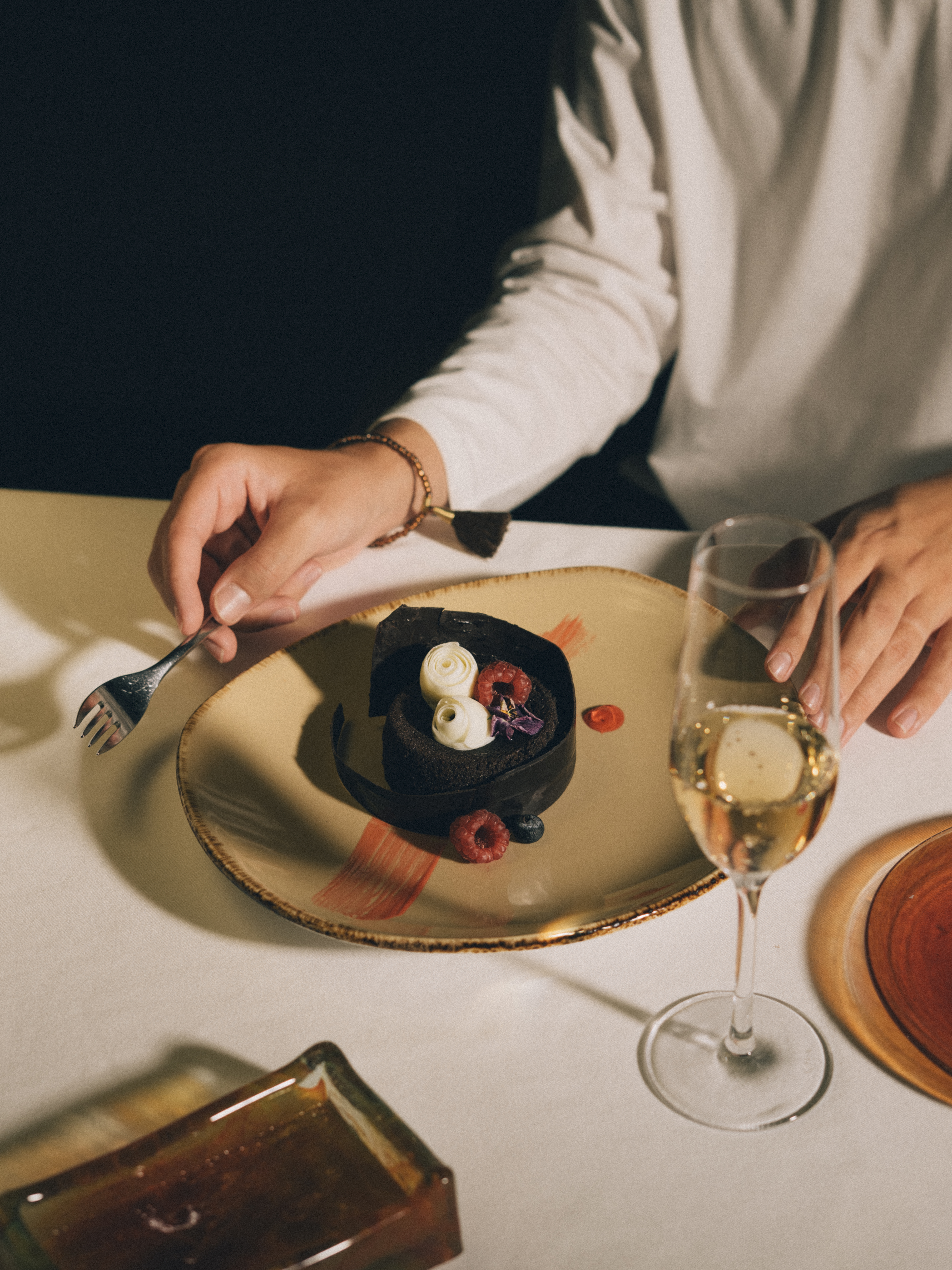 Elegant chocolate dessert with berries and cream, person with fork and champagne.