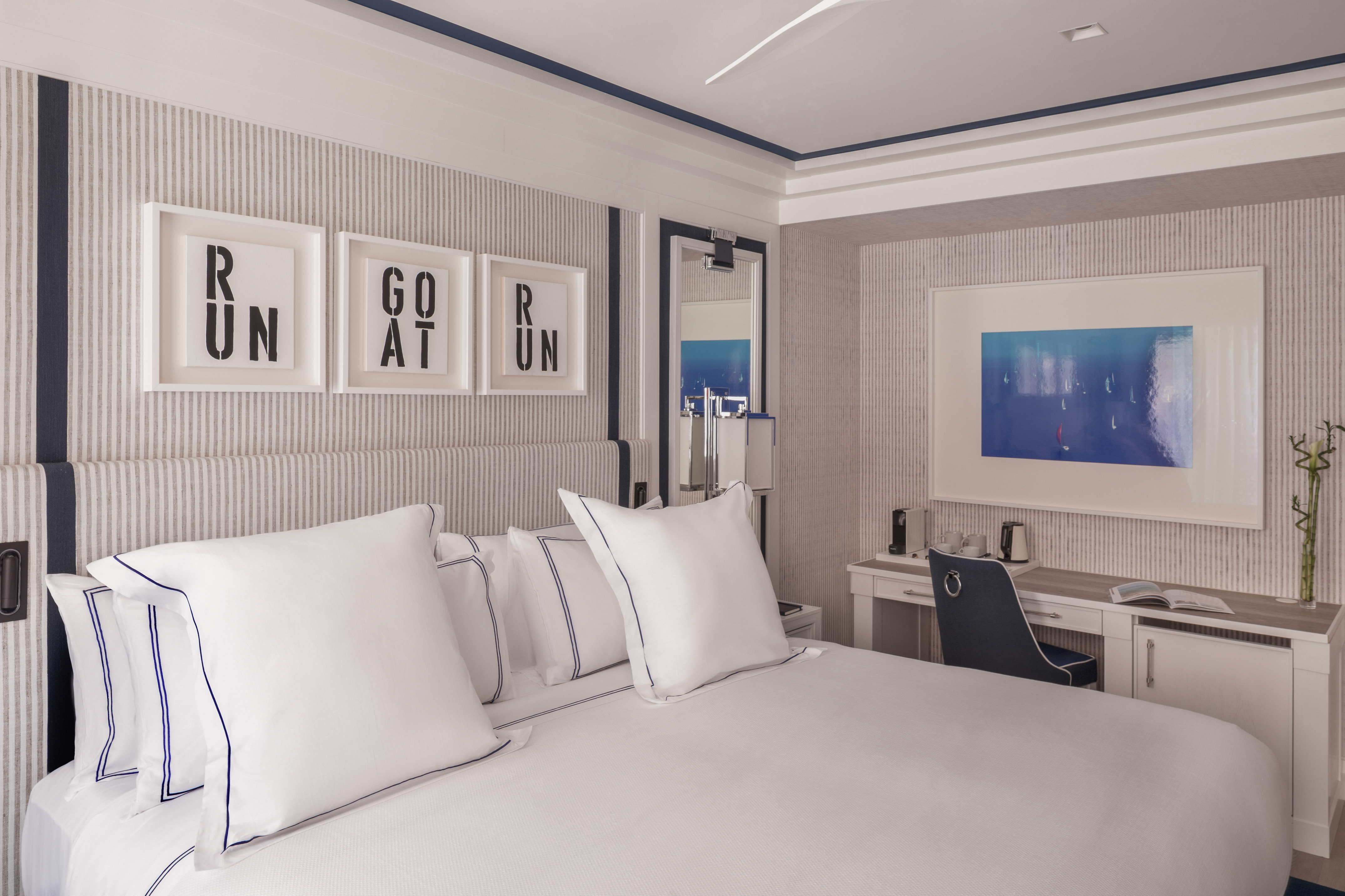 Modern white/navy bedroom with striped walls, bed, desk, and framed art.