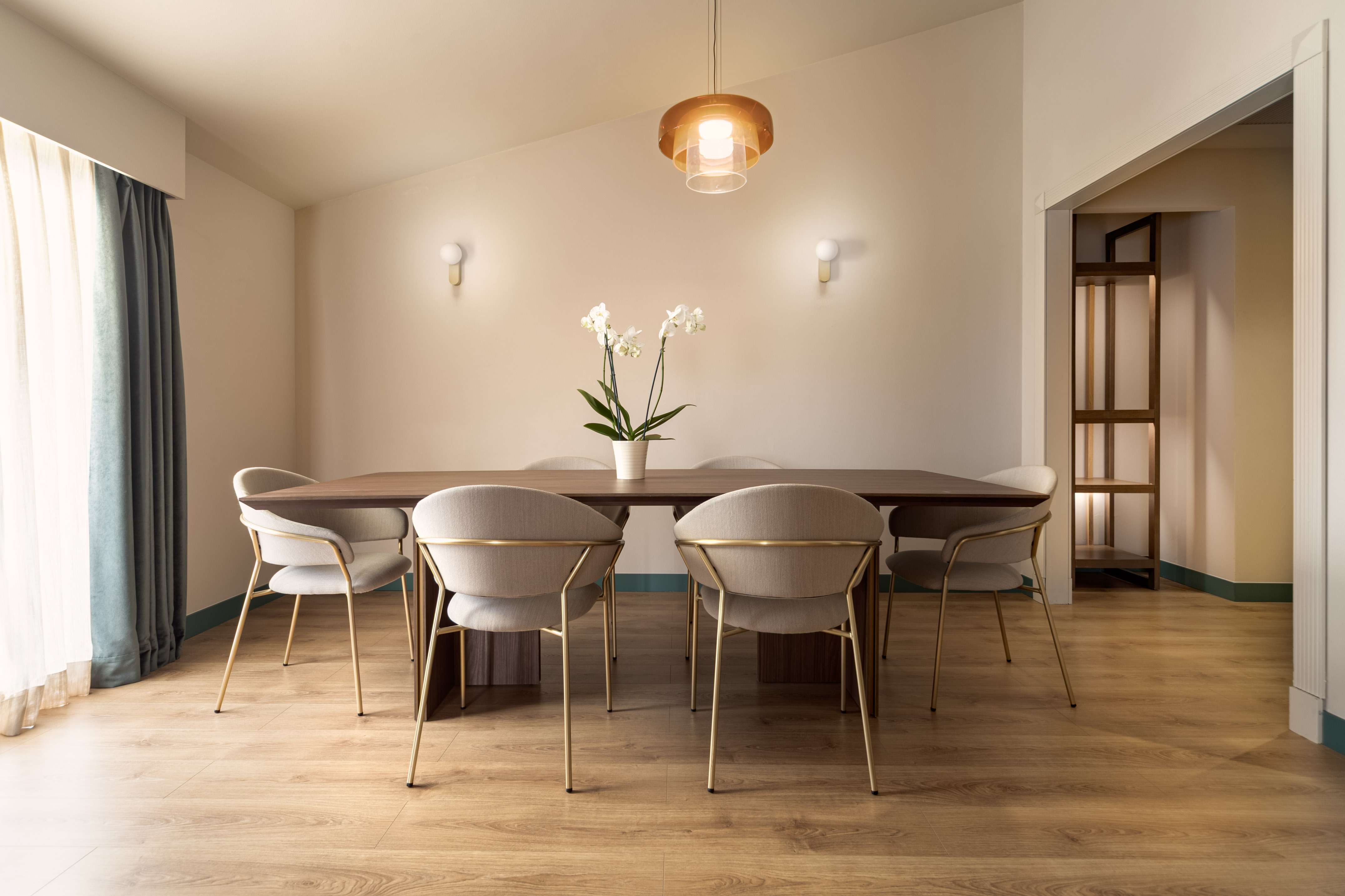Dining room with modern wood table, 6 beige chairs, orchid, and pendant light.