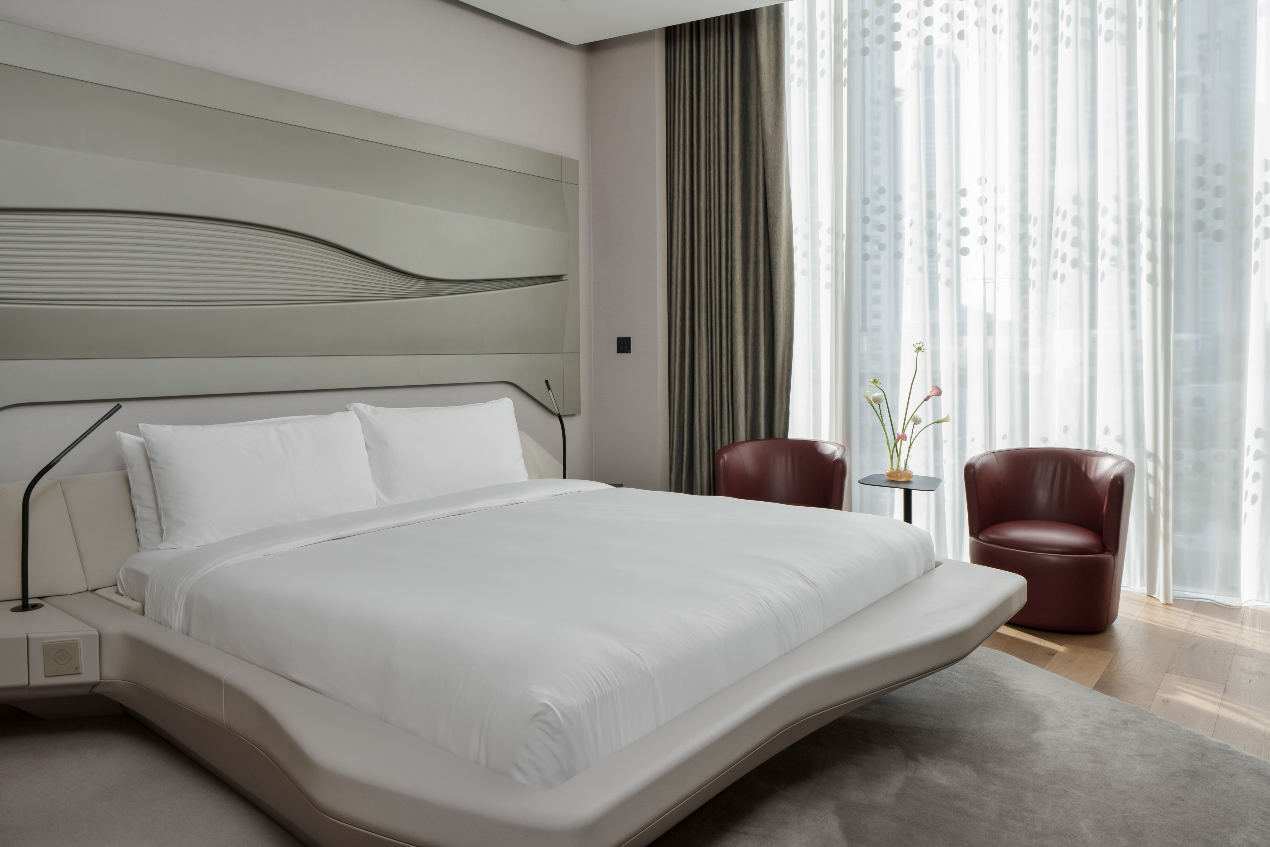 Sleek modern hotel bedroom with king bed, curved headboard, and accent chairs.